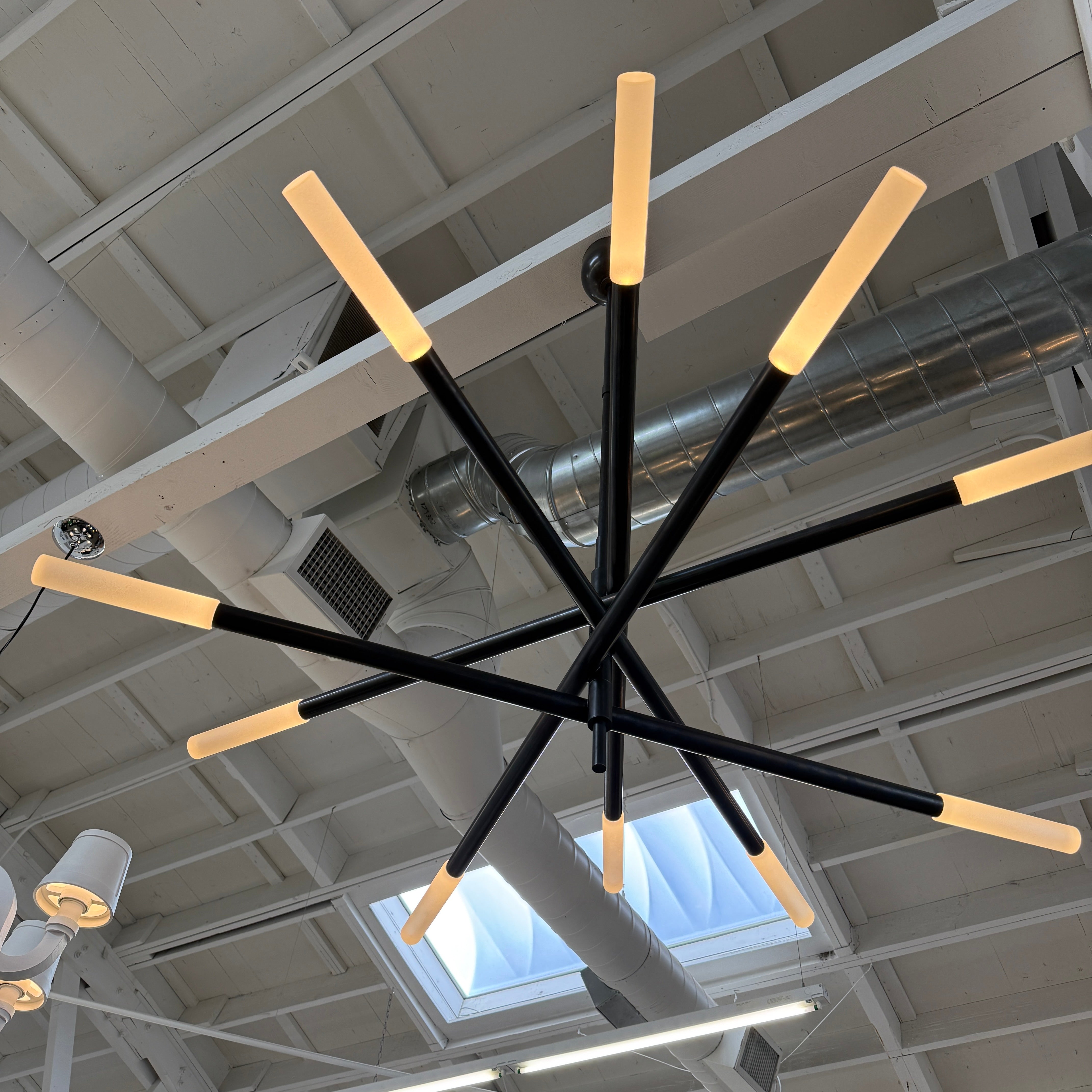 The Visual Comfort Signature Rousseau Grande Ten Light Articulating Chandelier features a modern black design with ten horizontal arms, each ending in a yellow-toned rectangular light, suspended from a central black rod against a white background.