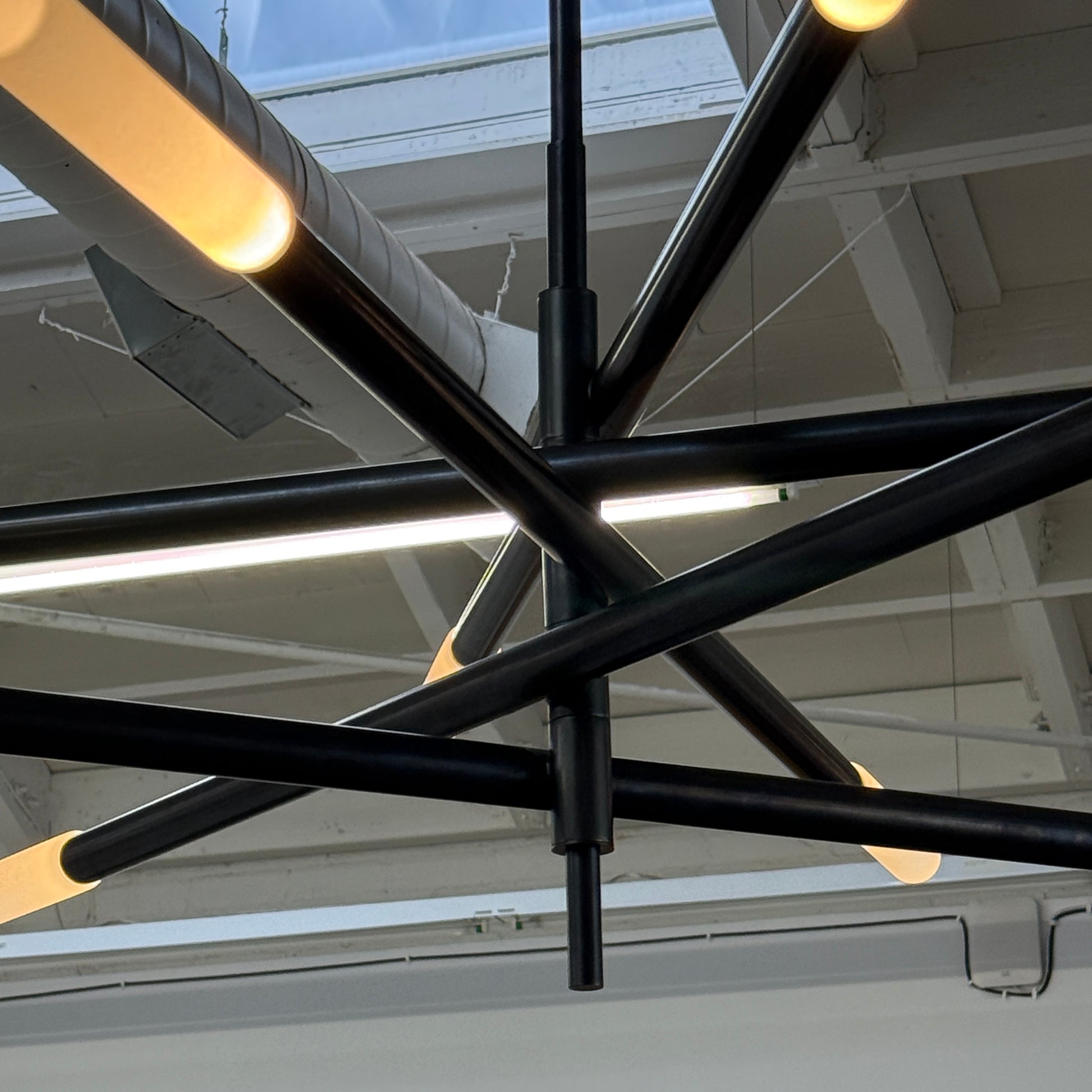 The Visual Comfort Signature Rousseau Grande Ten Light Articulating Chandelier features a modern black design with ten horizontal arms, each ending in a yellow-toned rectangular light, suspended from a central black rod against a white background.