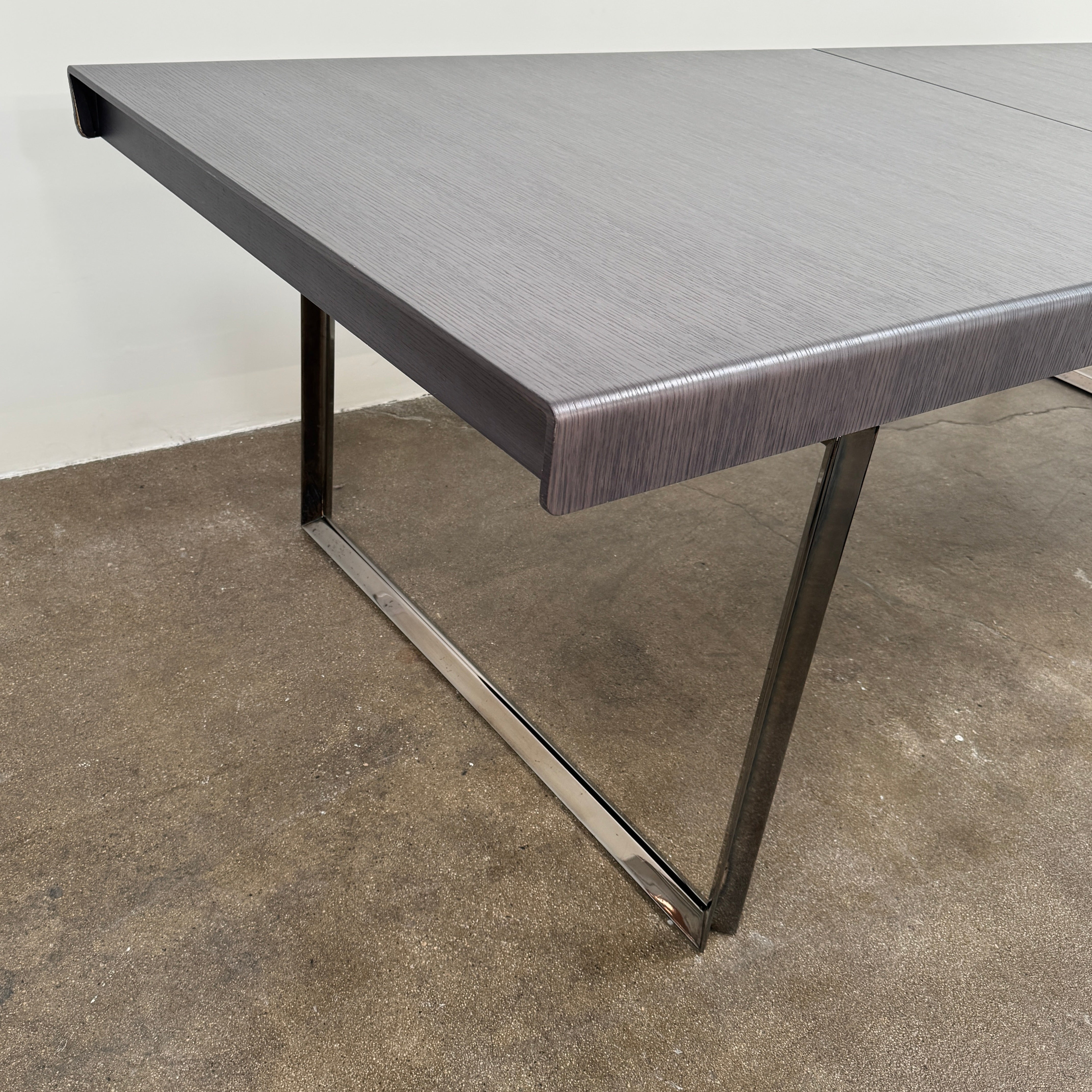 The B&B Italia Athos 12 Extendable Dining Table by Paolo Piva features a sleek rectangular dark gray top and black metal legs, showcased against a plain white background.