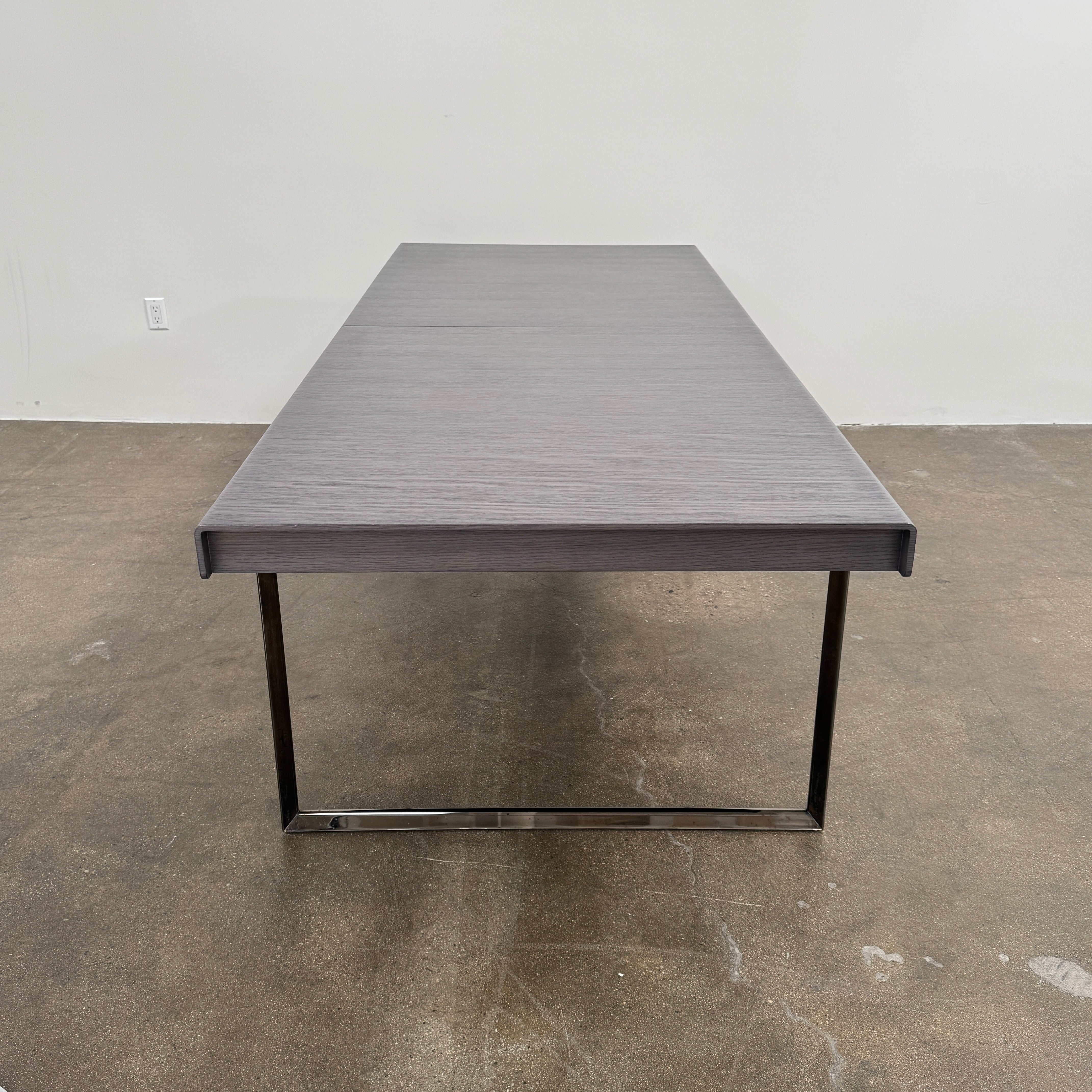 The B&B Italia Athos 12 Extendable Dining Table by Paolo Piva features a sleek rectangular dark gray top and black metal legs, showcased against a plain white background.