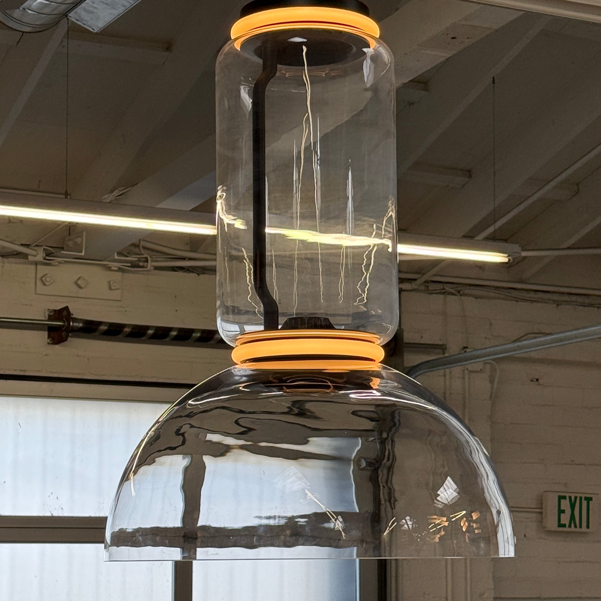 The Flos Noctambule Low Cylinder and Bowl LED Pendant 1 by Flos features a transparent blown crystal glass shade with a cylindrical glass element, suspended from the ceiling by a black cord.