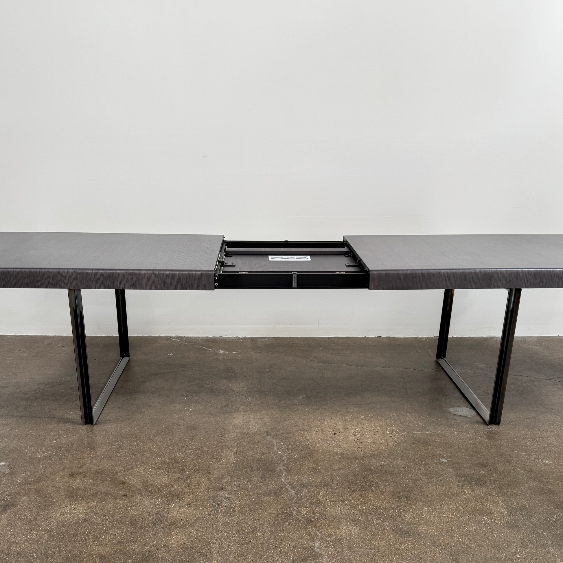 The B&B Italia Athos 12 Extendable Dining Table by Paolo Piva features a sleek rectangular dark gray top and black metal legs, showcased against a plain white background.