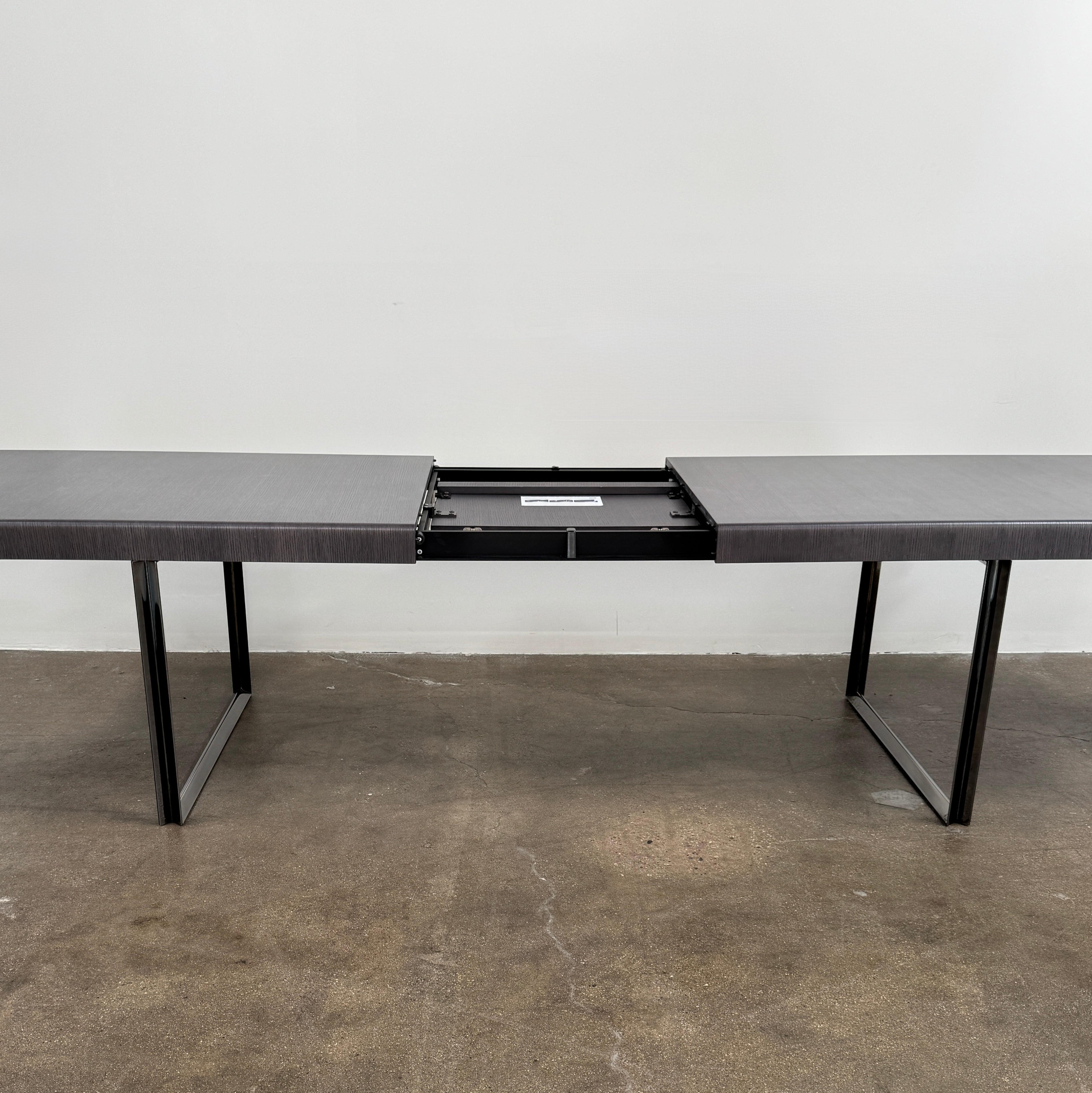 The B&B Italia Athos 12 Extendable Dining Table by Paolo Piva features a sleek rectangular dark gray top and black metal legs, showcased against a plain white background.