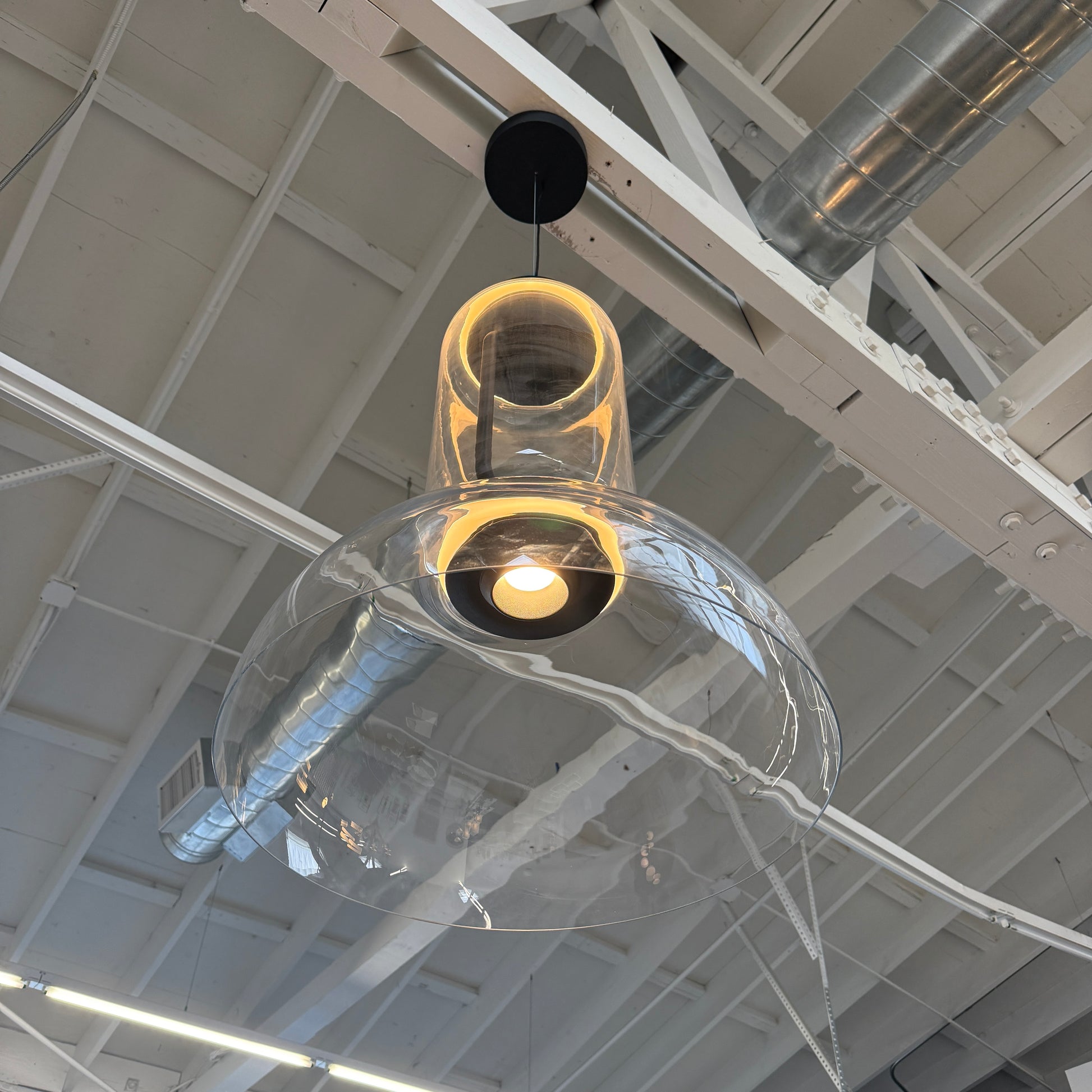 The Flos Noctambule Low Cylinder and Bowl LED Pendant 1 by Flos features a transparent blown crystal glass shade with a cylindrical glass element, suspended from the ceiling by a black cord.