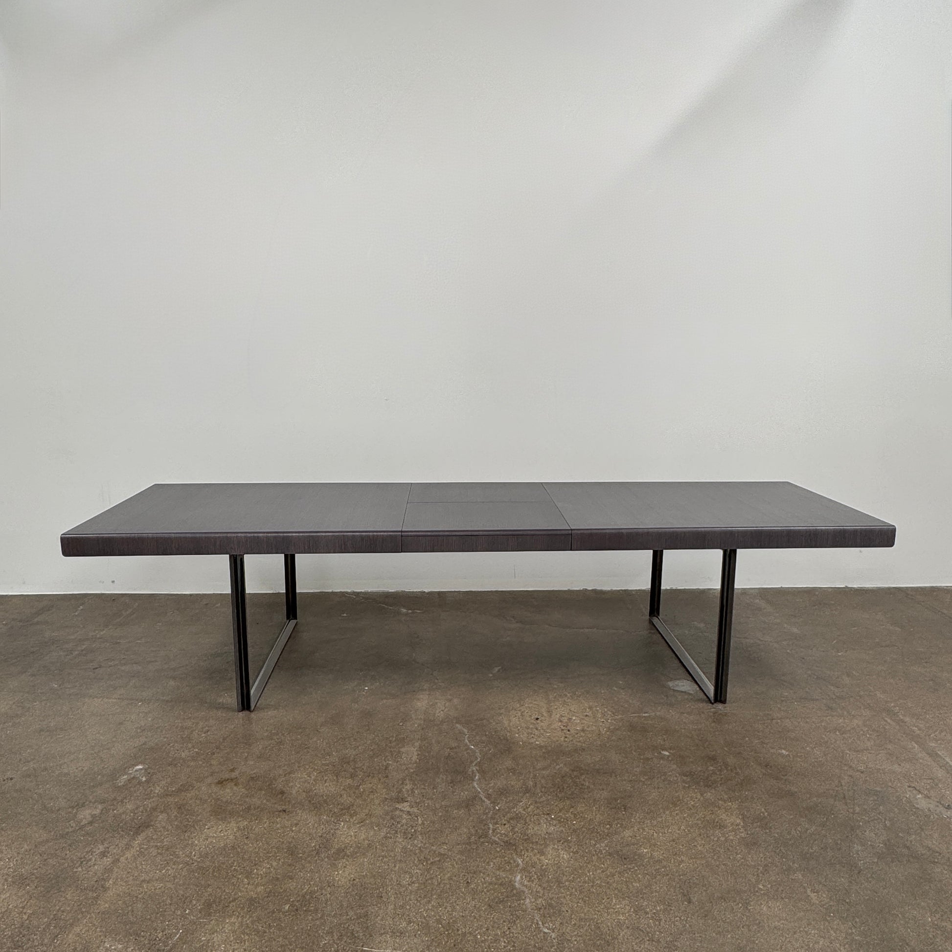 The B&B Italia Athos 12 Extendable Dining Table by Paolo Piva features a sleek rectangular dark gray top and black metal legs, showcased against a plain white background.