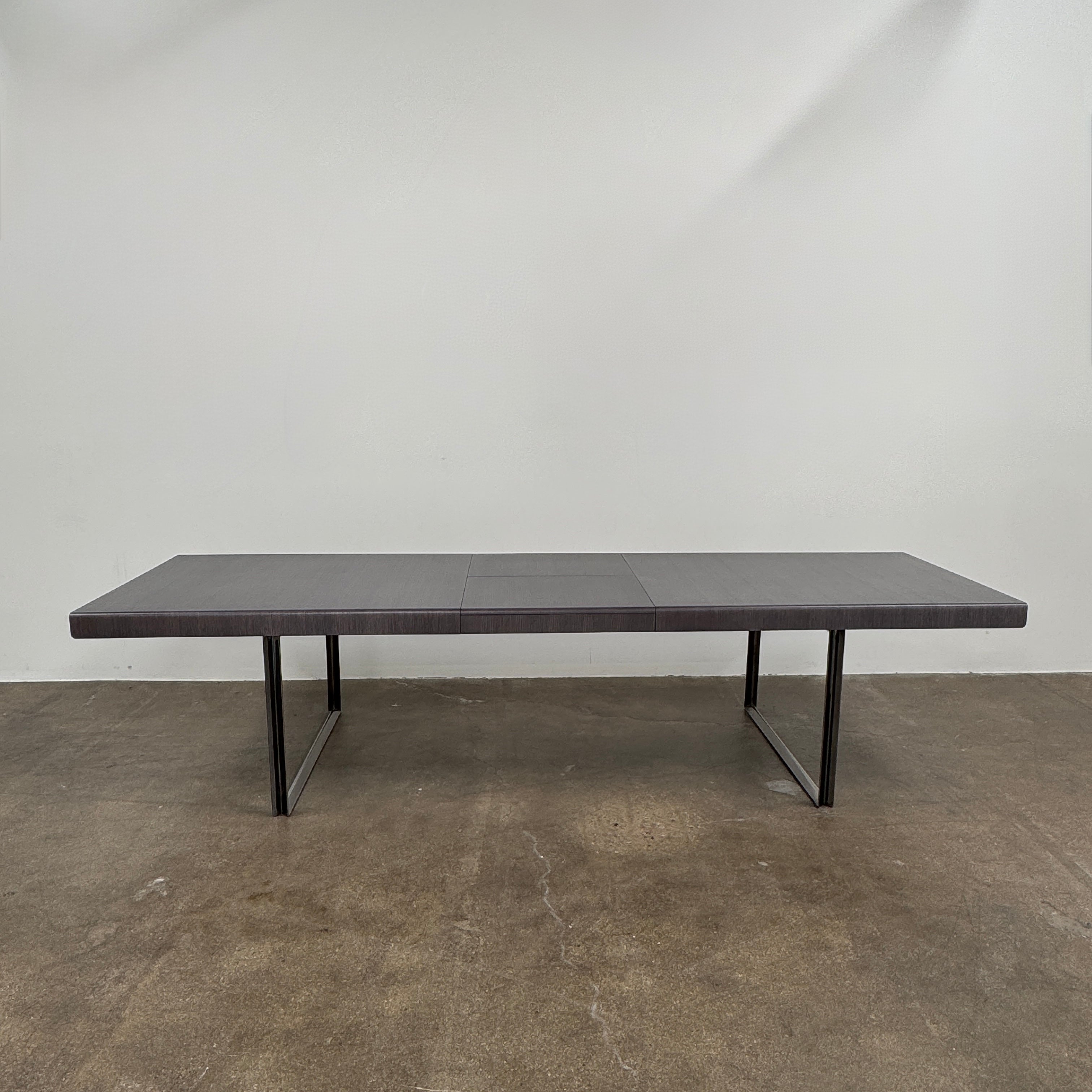 The B&B Italia Athos 12 Extendable Dining Table by Paolo Piva features a sleek rectangular dark gray top and black metal legs, showcased against a plain white background.