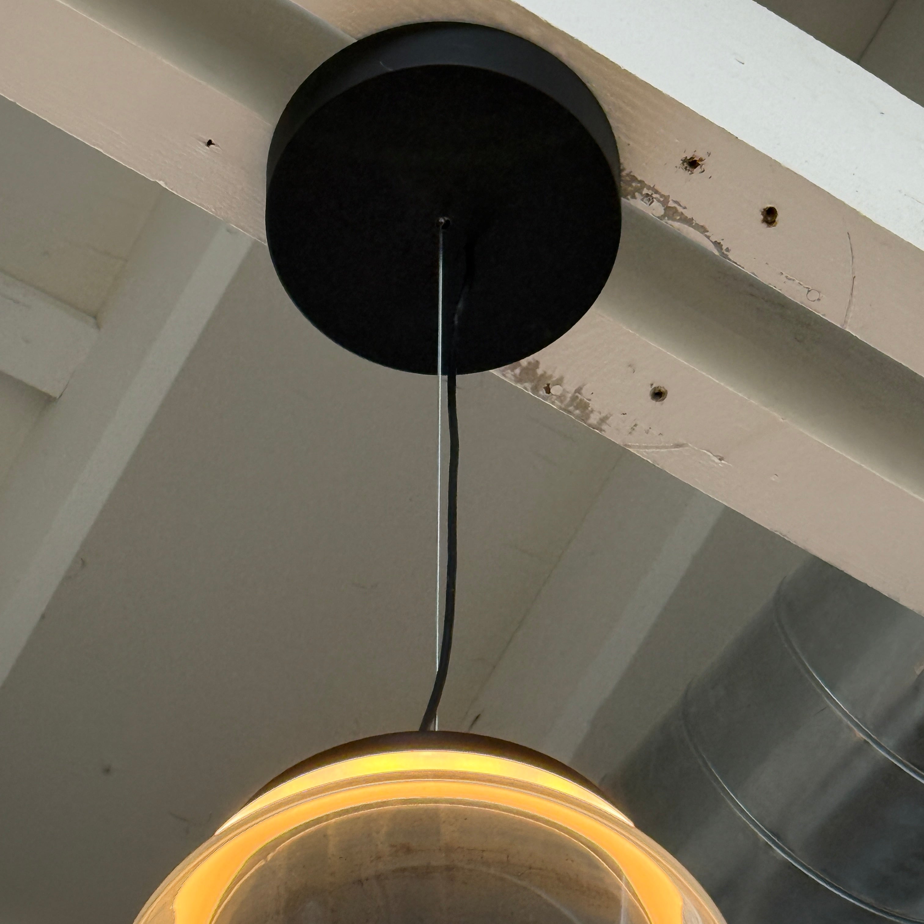 The Flos Noctambule Low Cylinder and Bowl LED Pendant 1 by Flos features a transparent blown crystal glass shade with a cylindrical glass element, suspended from the ceiling by a black cord.