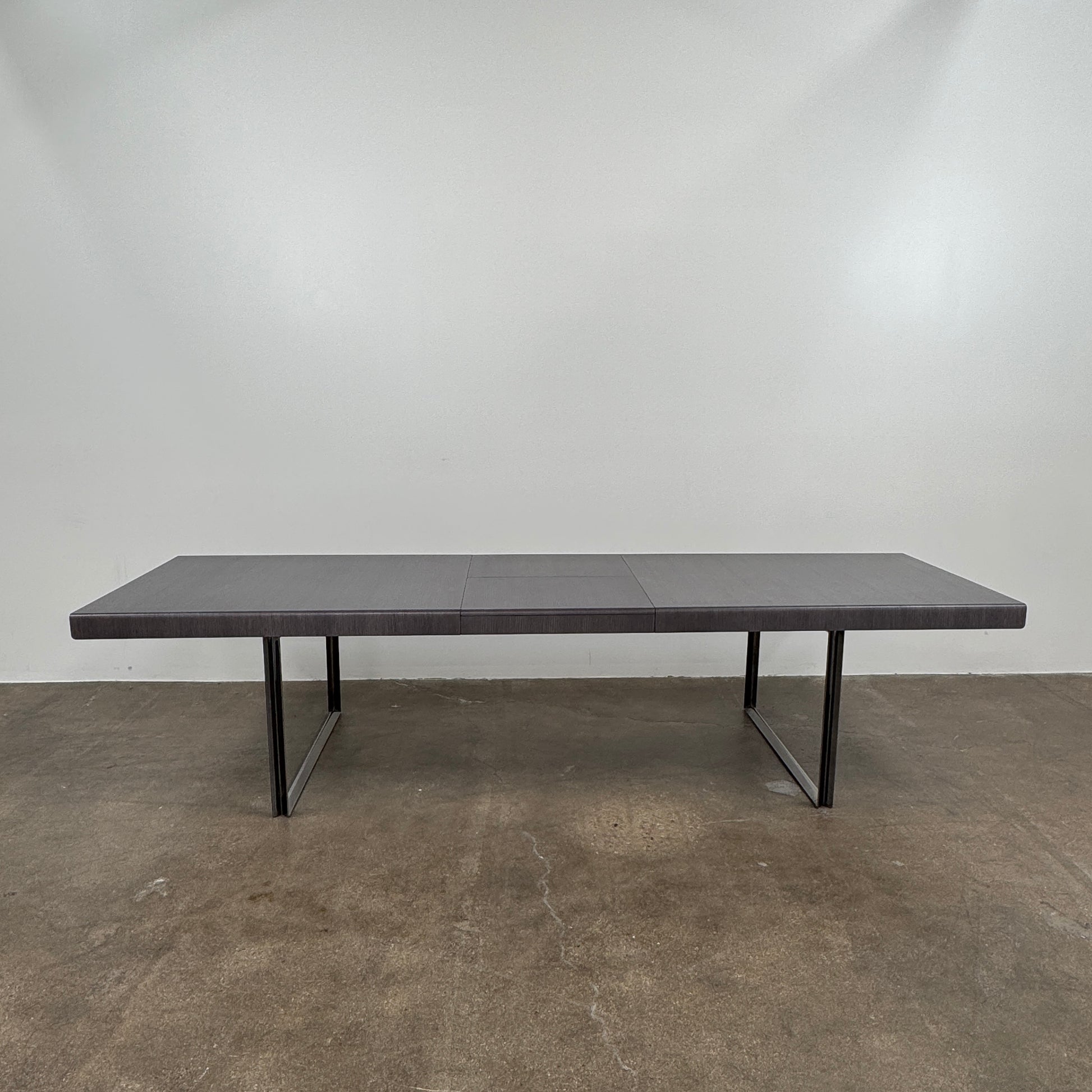 The B&B Italia Athos 12 Extendable Dining Table by Paolo Piva features a sleek rectangular dark gray top and black metal legs, showcased against a plain white background.