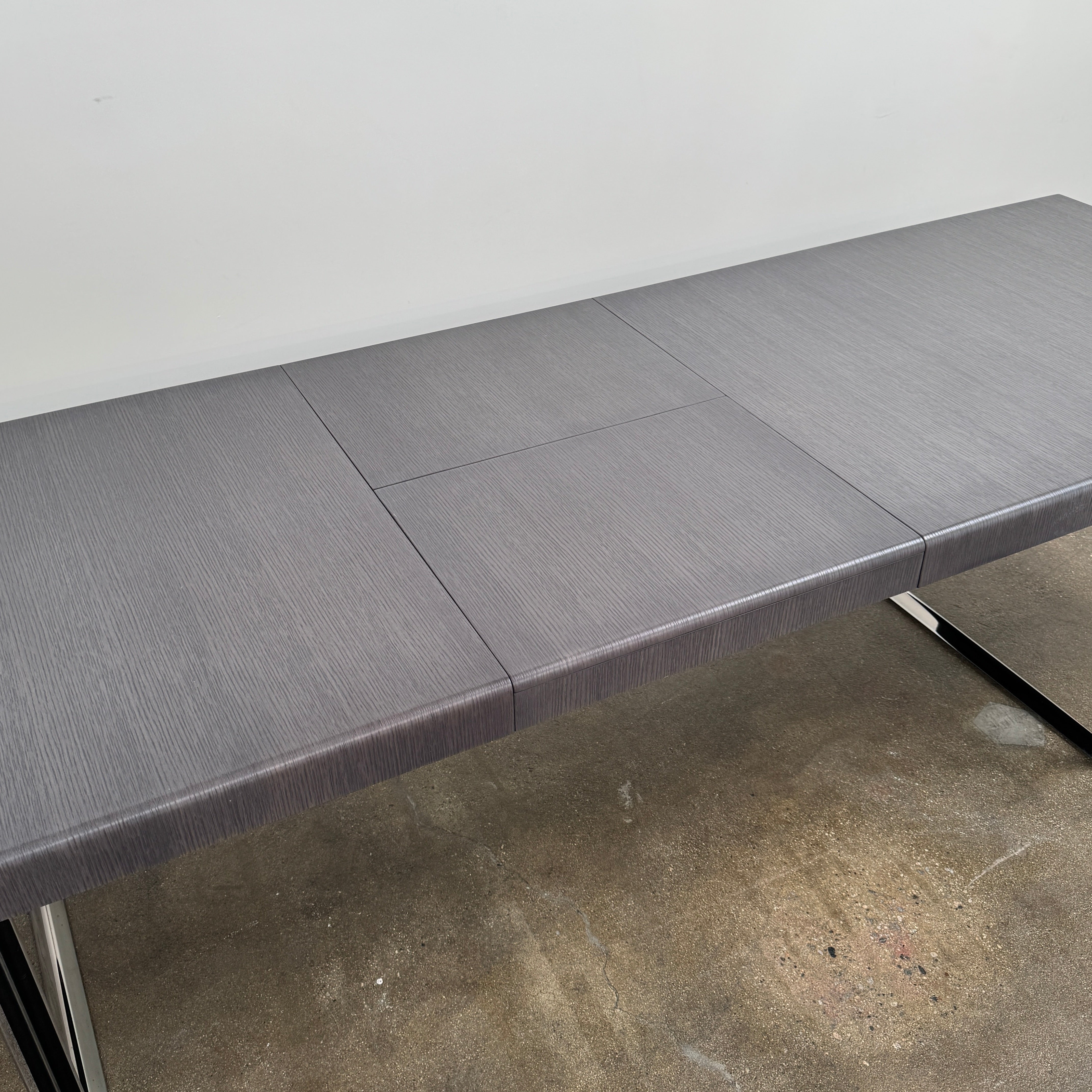 The B&B Italia Athos 12 Extendable Dining Table by Paolo Piva features a sleek rectangular dark gray top and black metal legs, showcased against a plain white background.