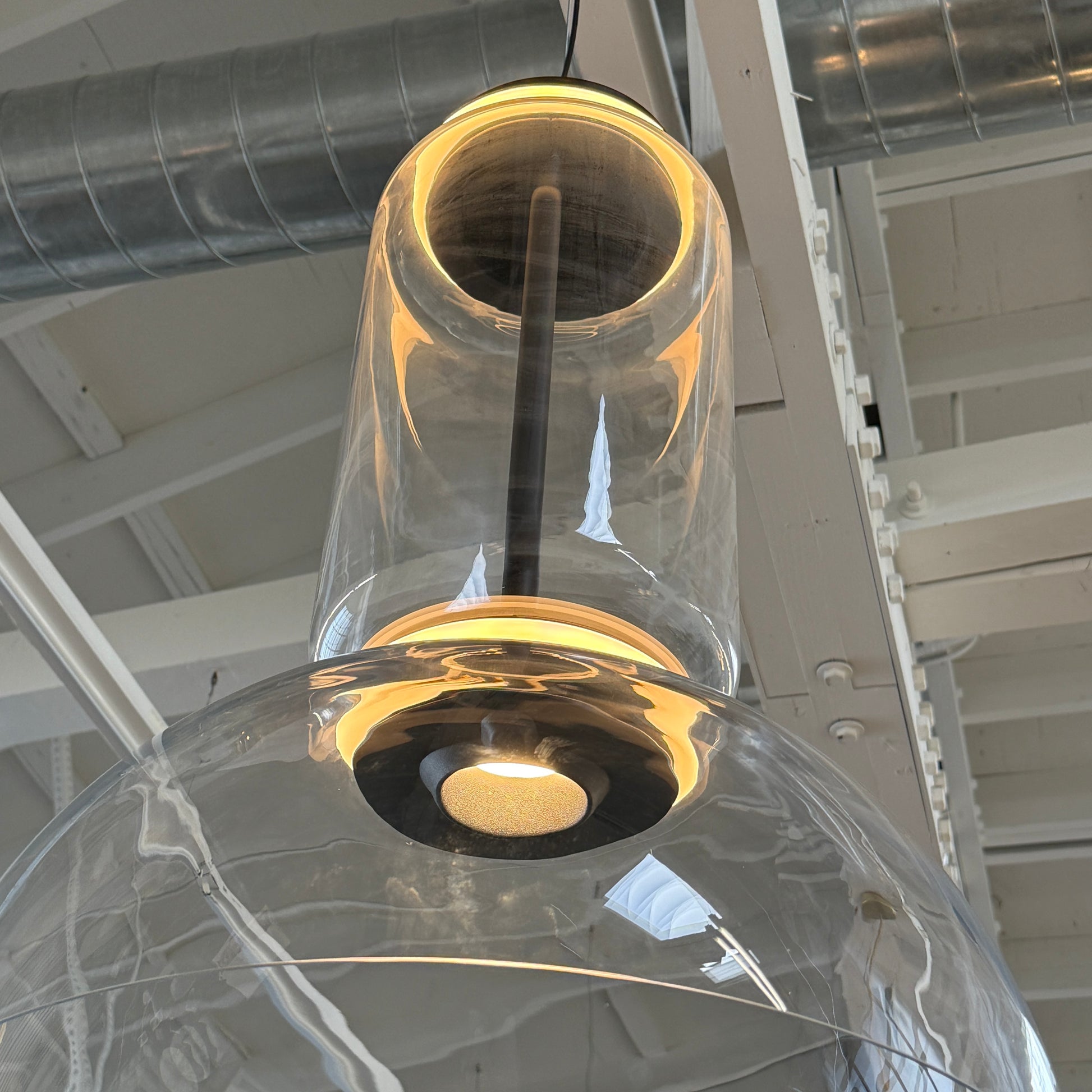 The Flos Noctambule Low Cylinder and Bowl LED Pendant 1 by Flos features a transparent blown crystal glass shade with a cylindrical glass element, suspended from the ceiling by a black cord.