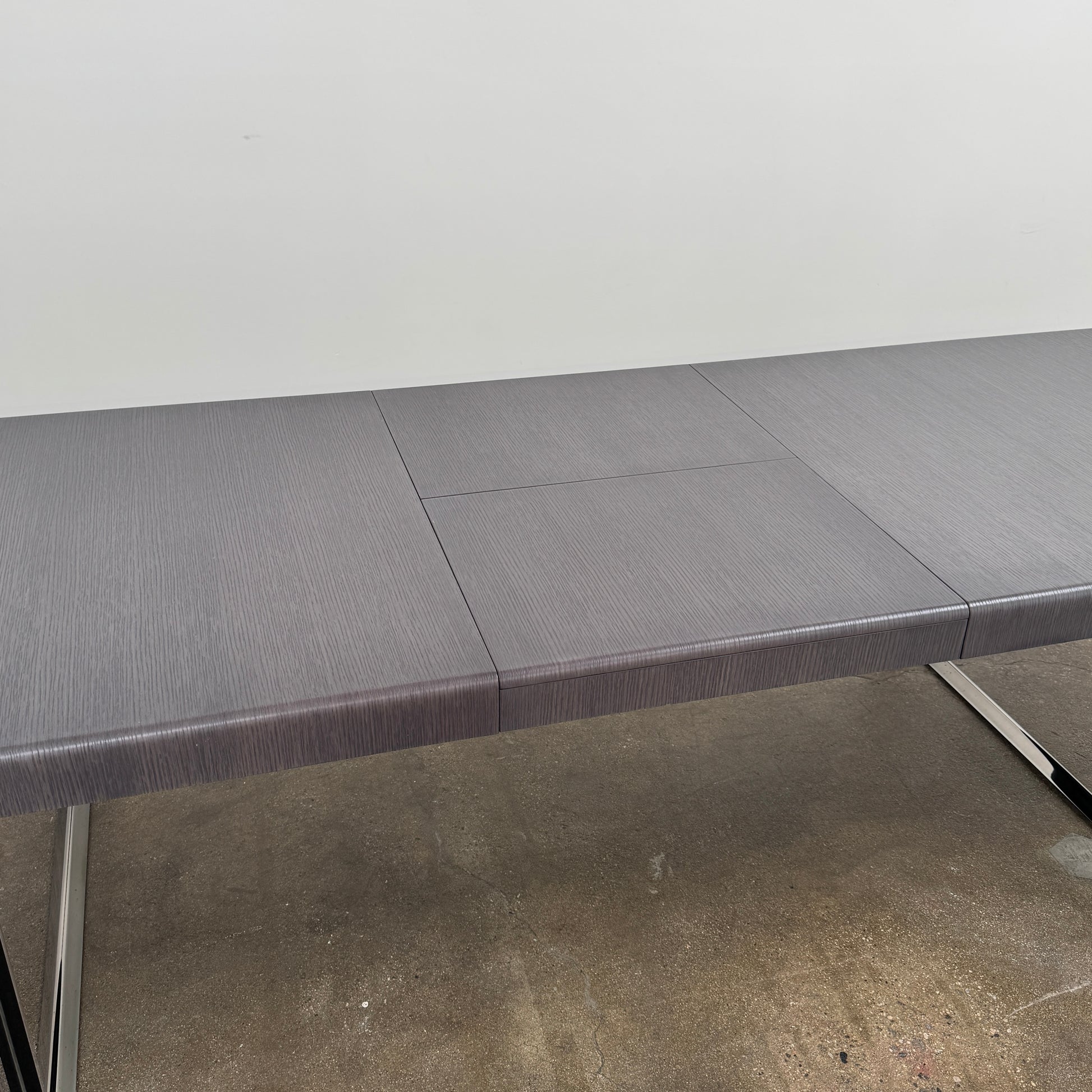 The B&B Italia Athos 12 Extendable Dining Table by Paolo Piva features a sleek rectangular dark gray top and black metal legs, showcased against a plain white background.