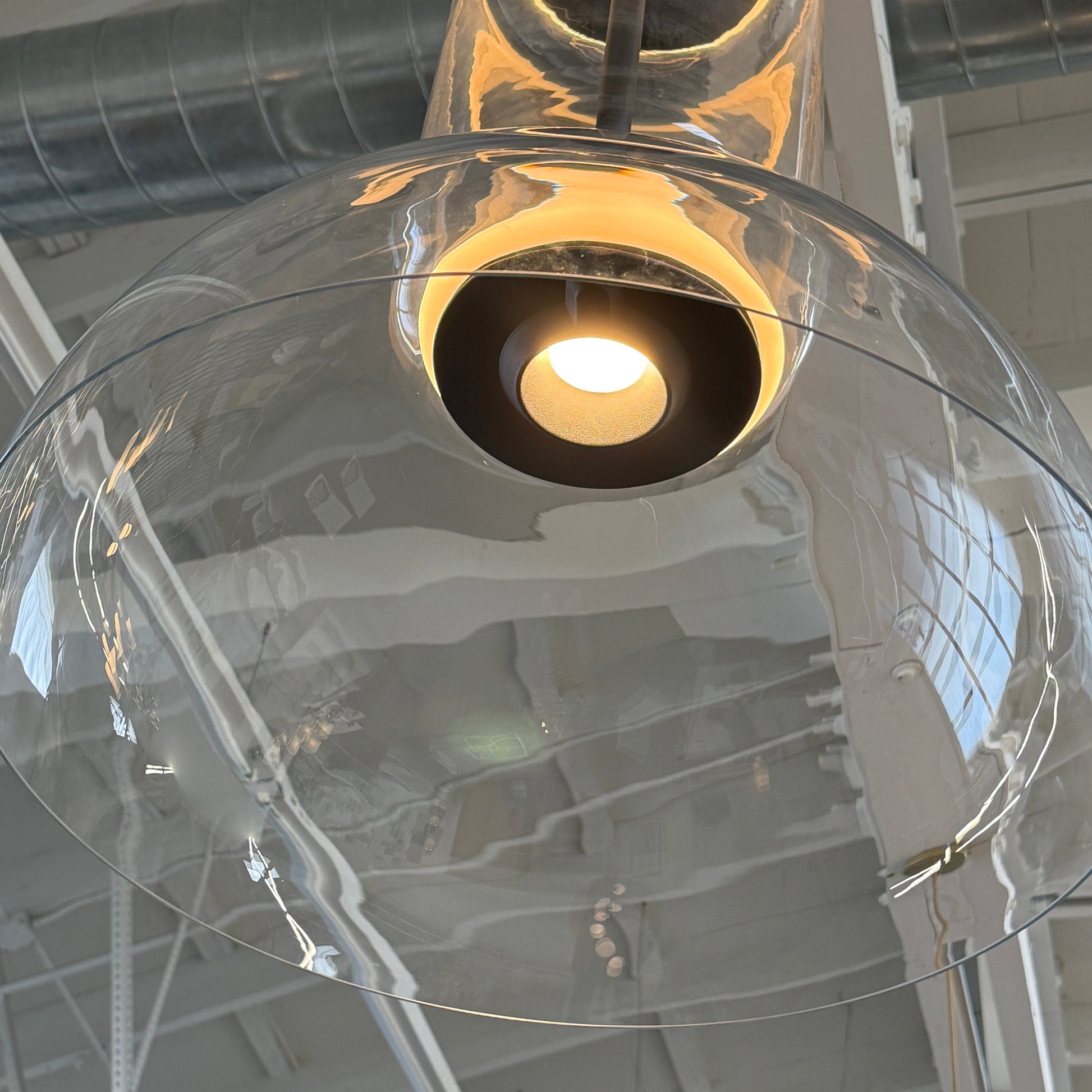 The Flos Noctambule Low Cylinder and Bowl LED Pendant 1 by Flos features a transparent blown crystal glass shade with a cylindrical glass element, suspended from the ceiling by a black cord.