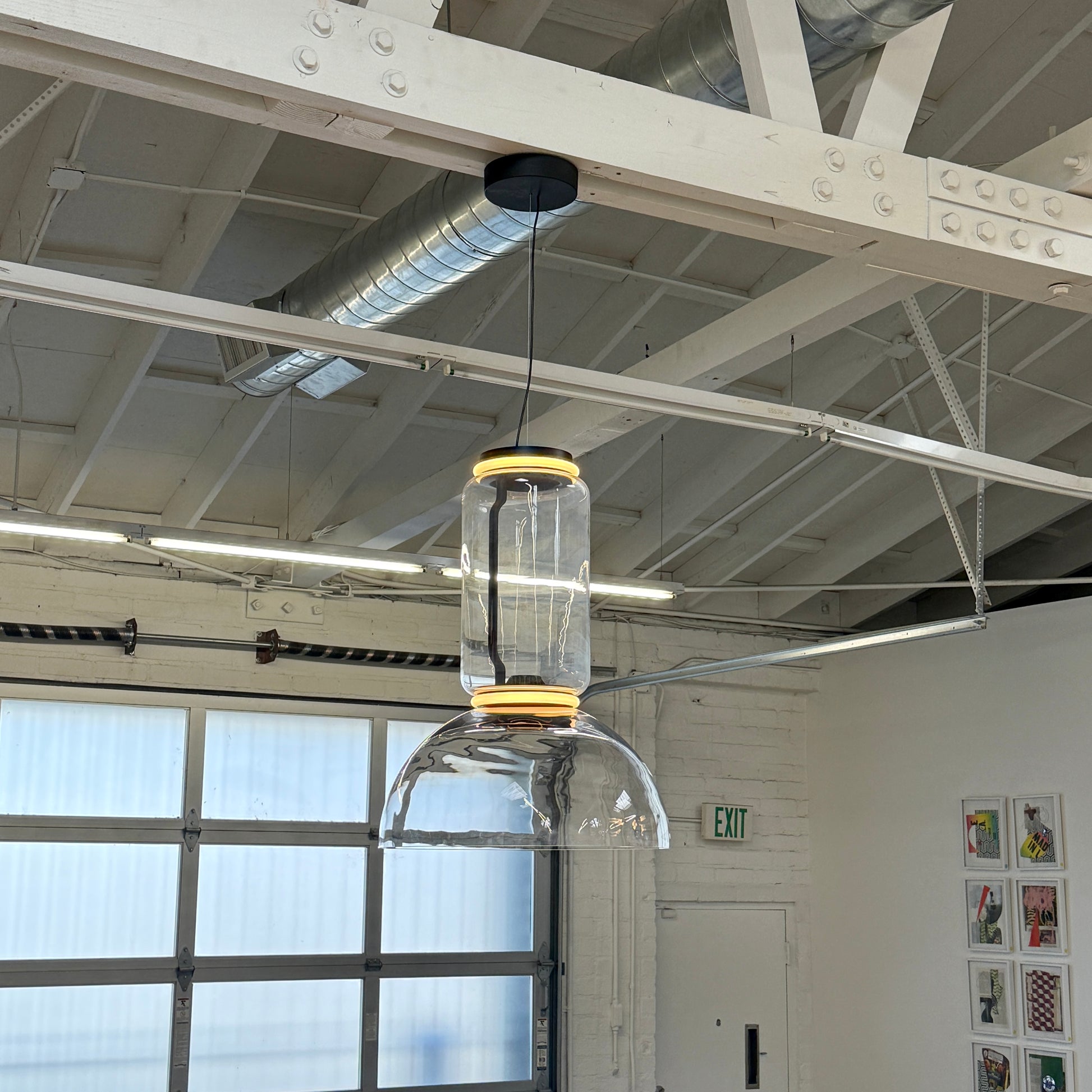 The Flos Noctambule Low Cylinder and Bowl LED Pendant 1 by Flos features a transparent blown crystal glass shade with a cylindrical glass element, suspended from the ceiling by a black cord.