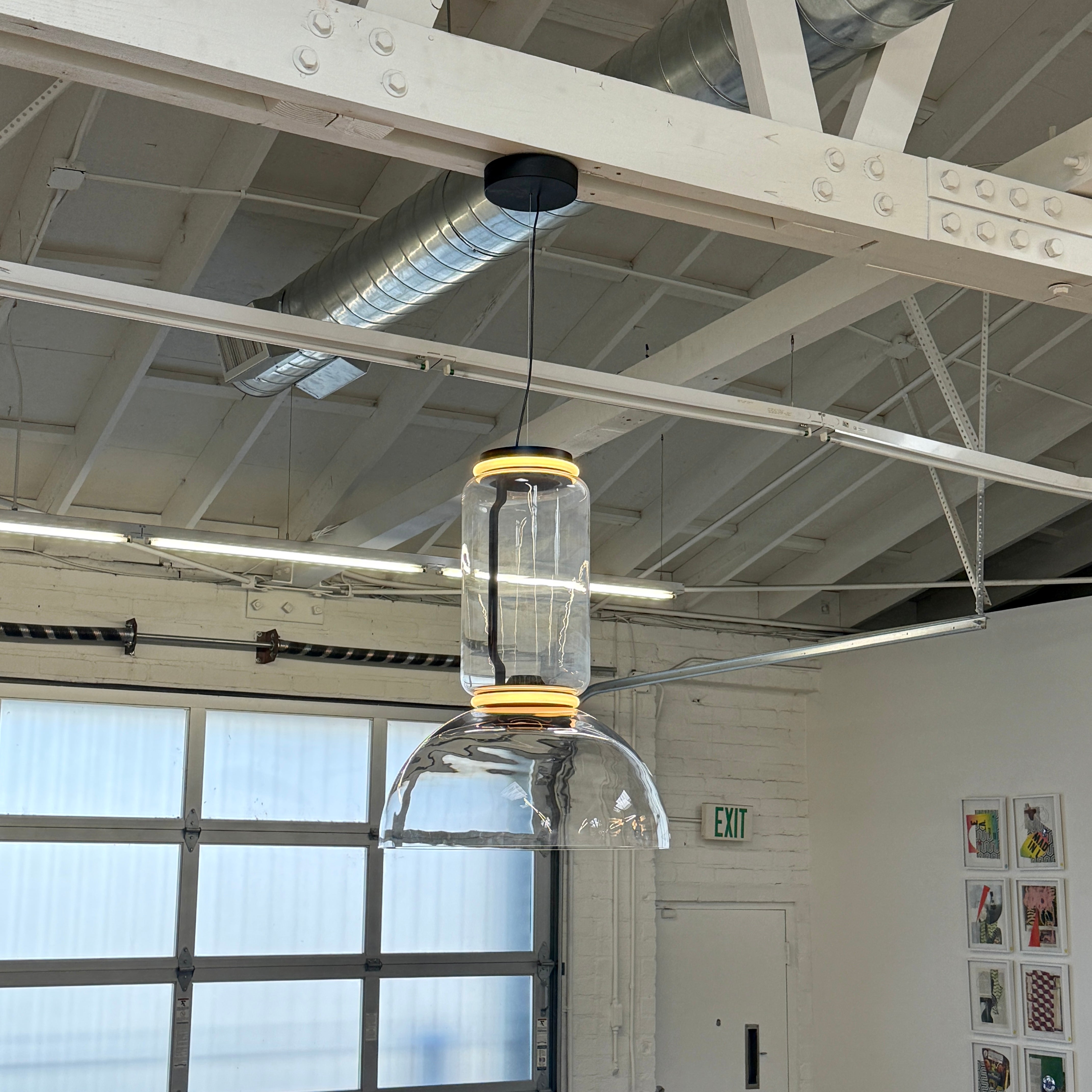 The Flos Noctambule Low Cylinder and Bowl LED Pendant 1 by Flos features a transparent blown crystal glass shade with a cylindrical glass element, suspended from the ceiling by a black cord.