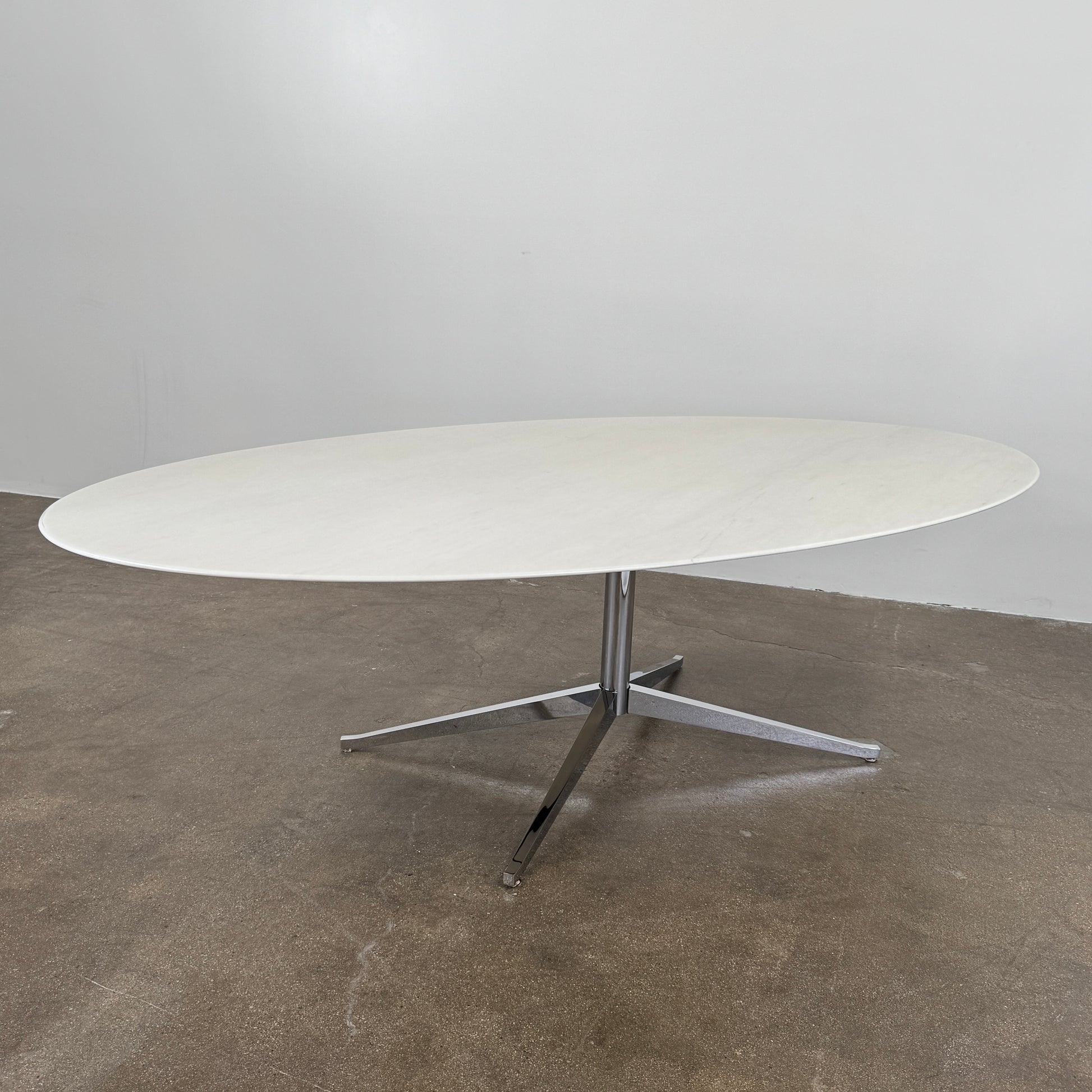 Florence Knoll’s DWR Florence Knoll Oval White Statuarietto Marble "Table Desk" features a slim marble top and black four-legged base, inspired by the iconic design, displayed against a plain white background.