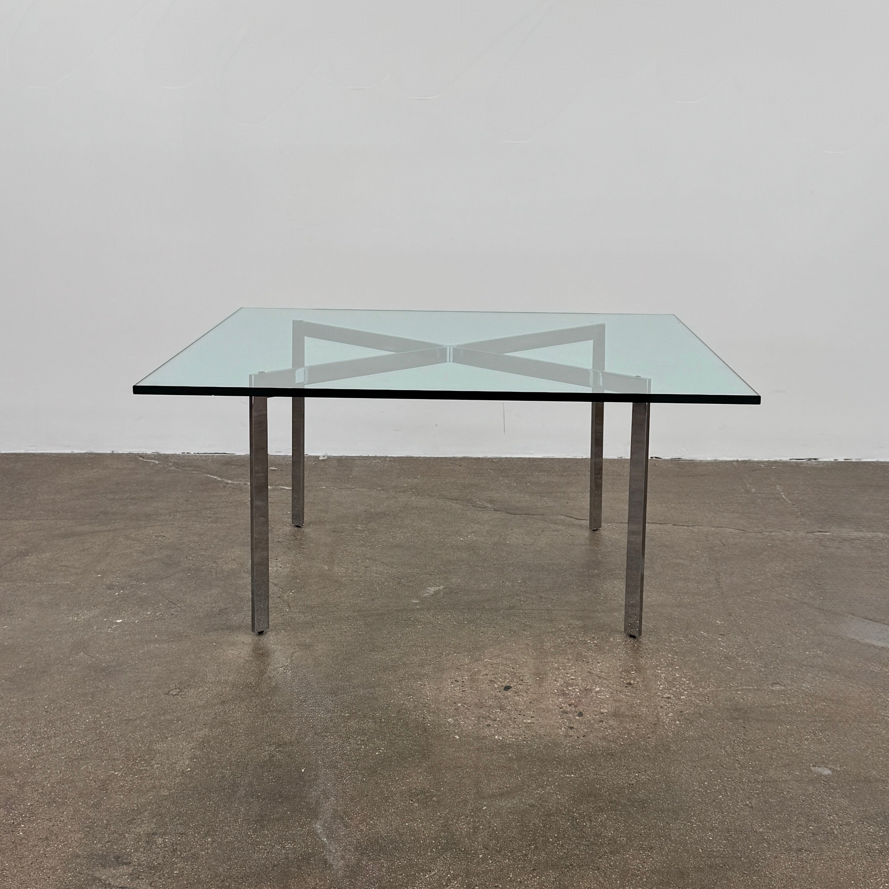 The Vintage DWR Barcelona Coffee Table by DWR features a rectangular glass top, four metal legs, and a visible metal support frame underneath.