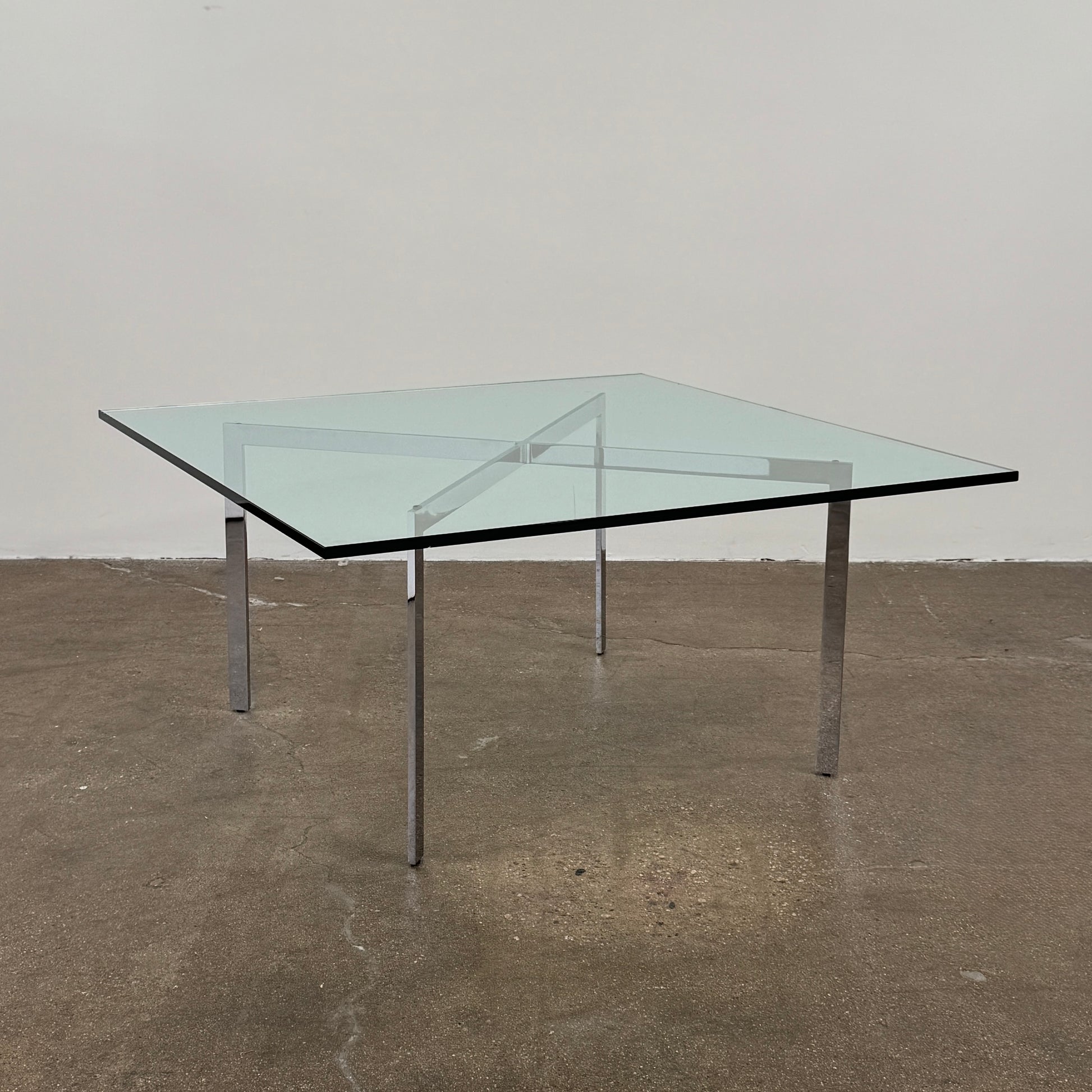 The Vintage DWR Barcelona Coffee Table by DWR features a rectangular glass top, four metal legs, and a visible metal support frame underneath.