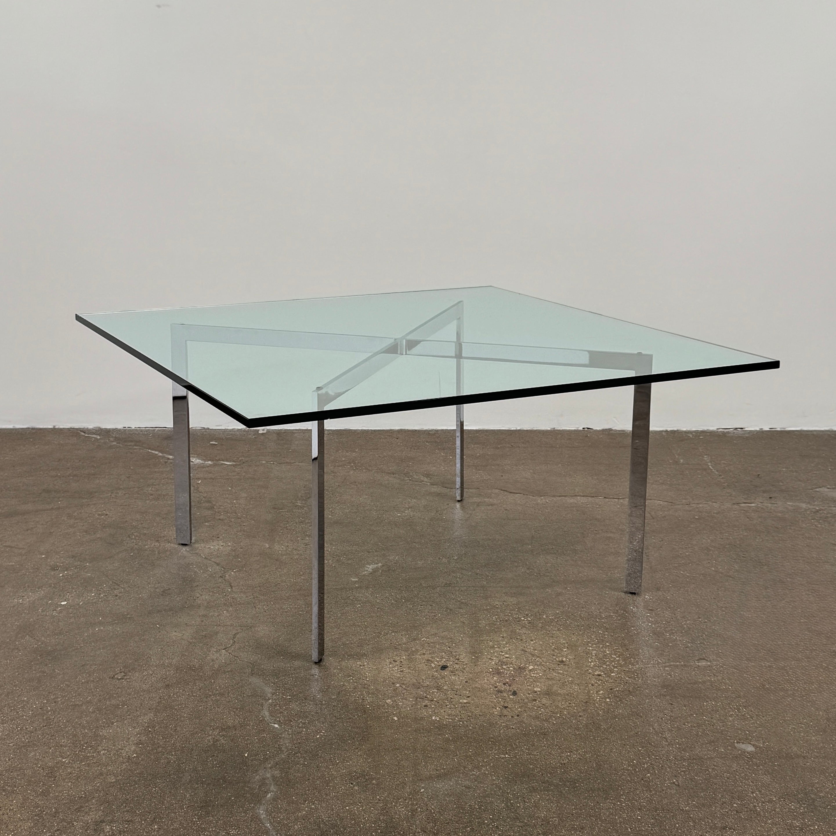 The Vintage DWR Barcelona Coffee Table by DWR features a rectangular glass top, four metal legs, and a visible metal support frame underneath.