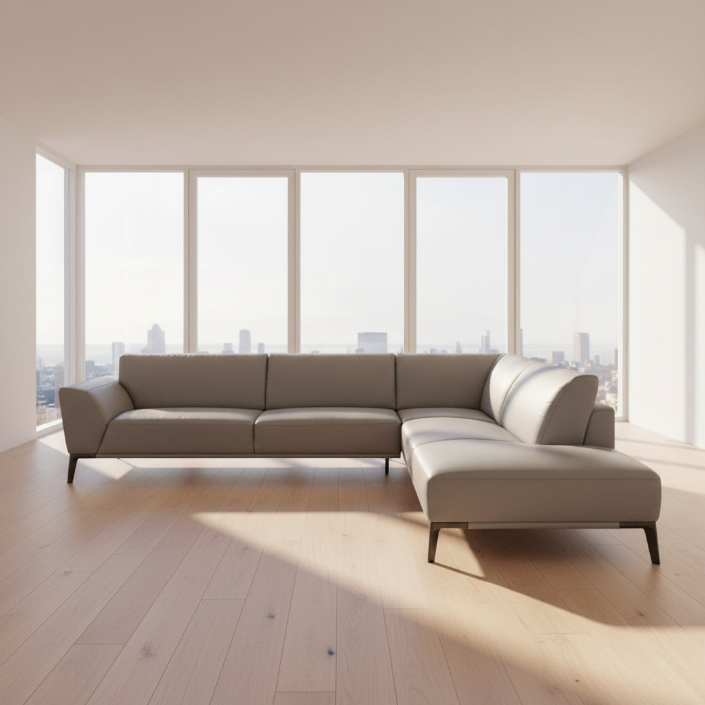 A Roche Bobois Accord Gray Leather Sectional sits in a spacious room with floor-to-ceiling windows and light wood floors, overlooking a cityscape.