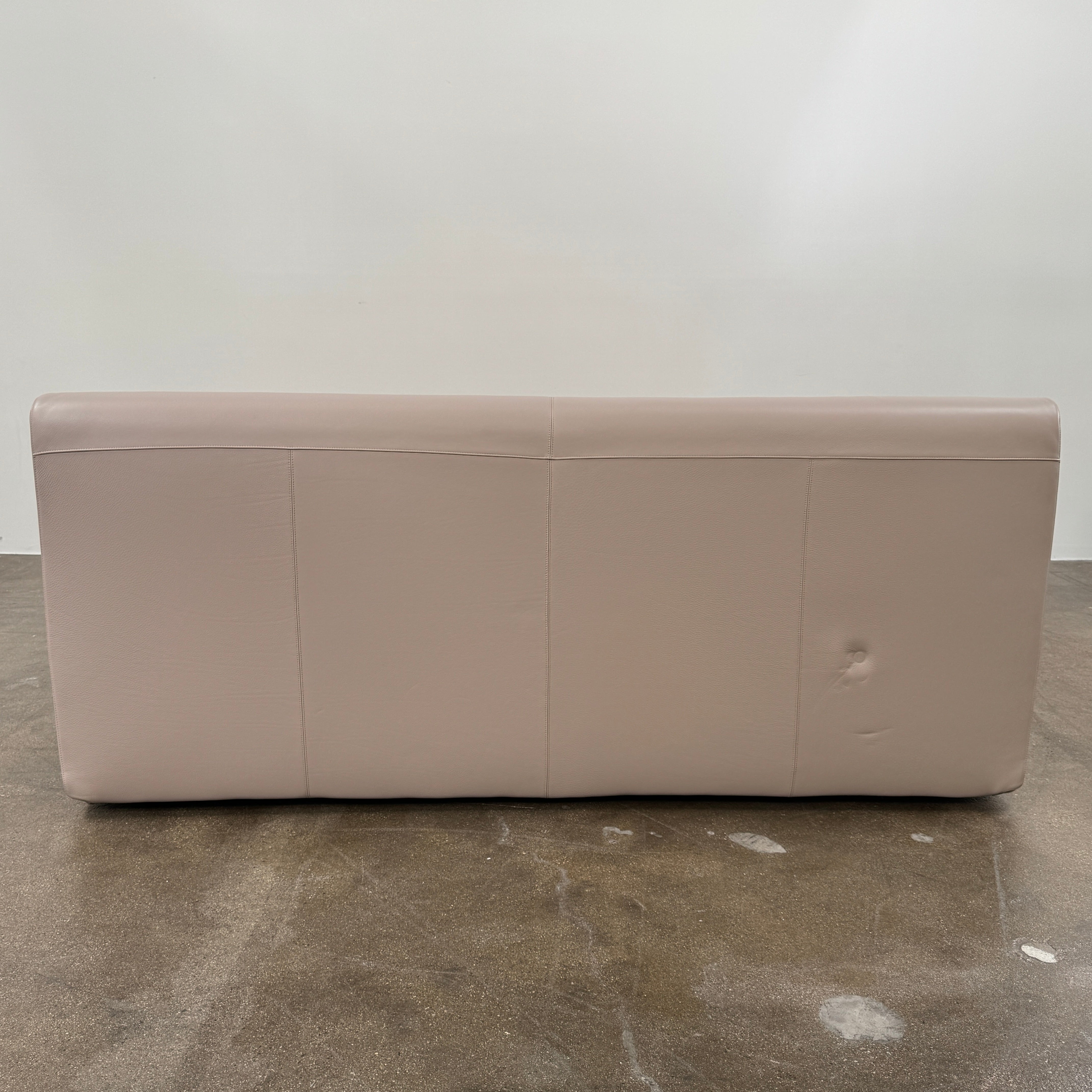The DWR Nest King Size Leather Bed features a beige upholstered headboard and base, exposed wooden slats, and a sturdy metal support structure for enhanced durability.