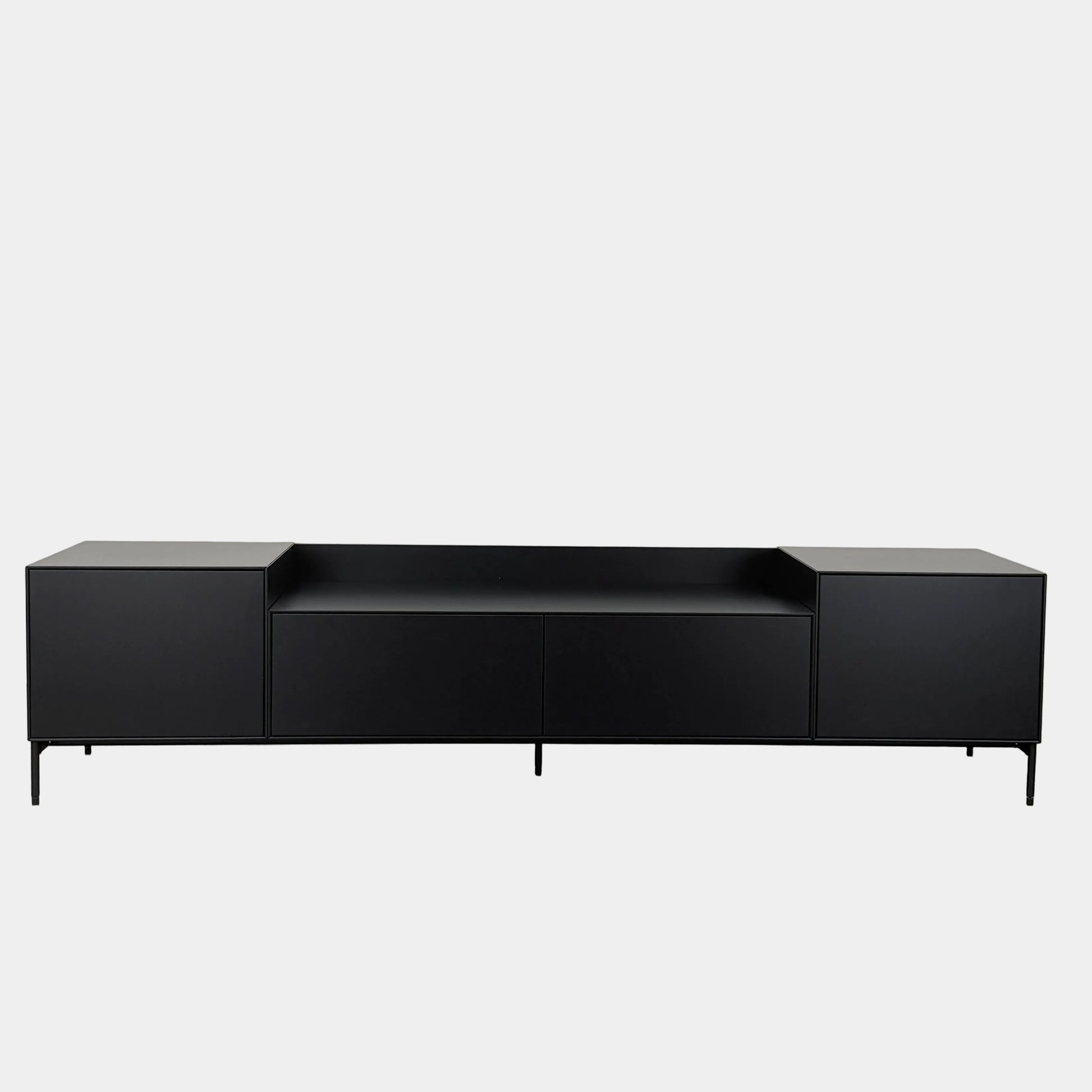 The Treku Lauki Media Unit by Treku features a black minimalist design with two closed side cabinets, two central drawers, an open shelf, and built-in cord management on slim metal legs—perfect for modern spaces.