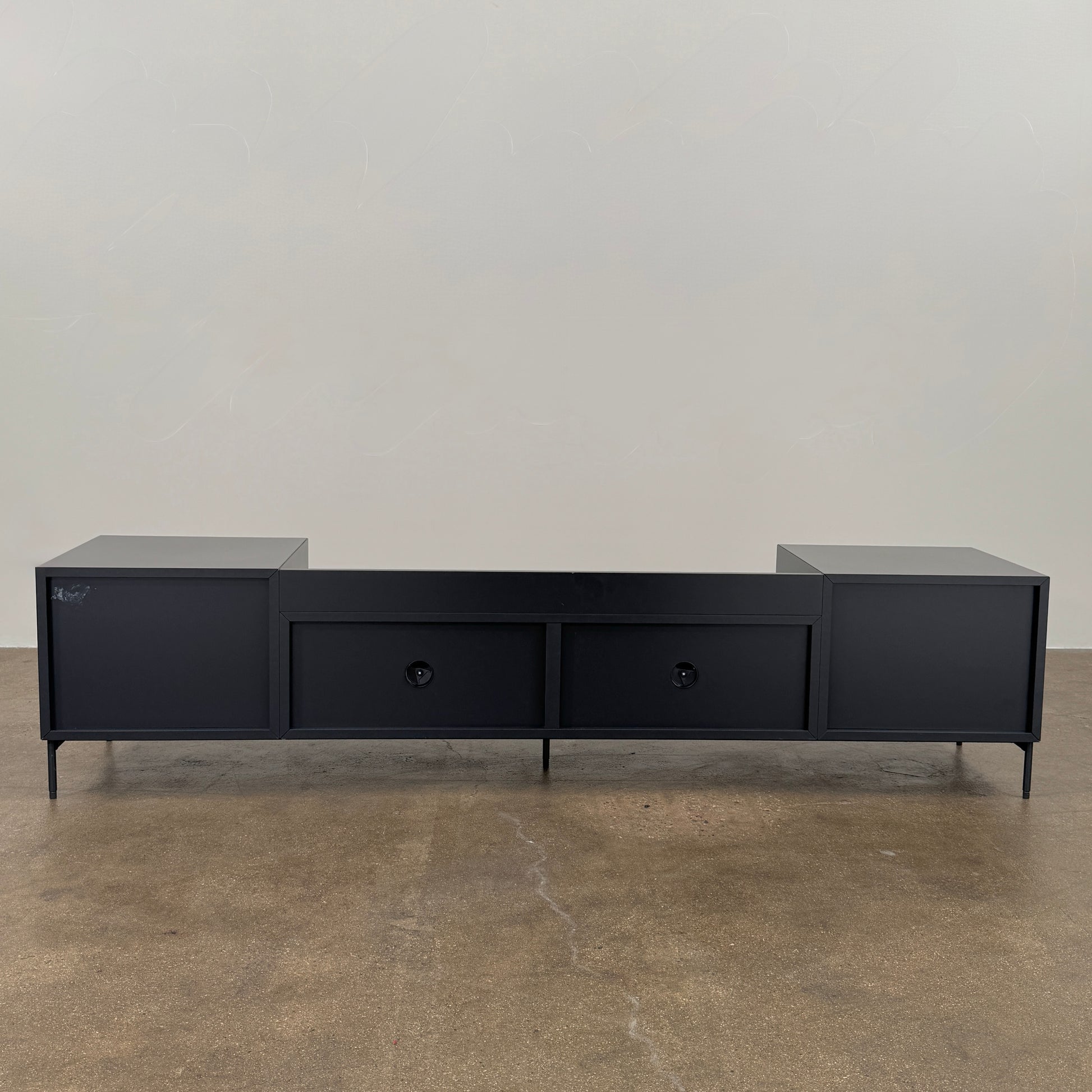 The Treku Lauki Media Unit by Treku features a black minimalist design with two closed side cabinets, two central drawers, an open shelf, and built-in cord management on slim metal legs—perfect for modern spaces.