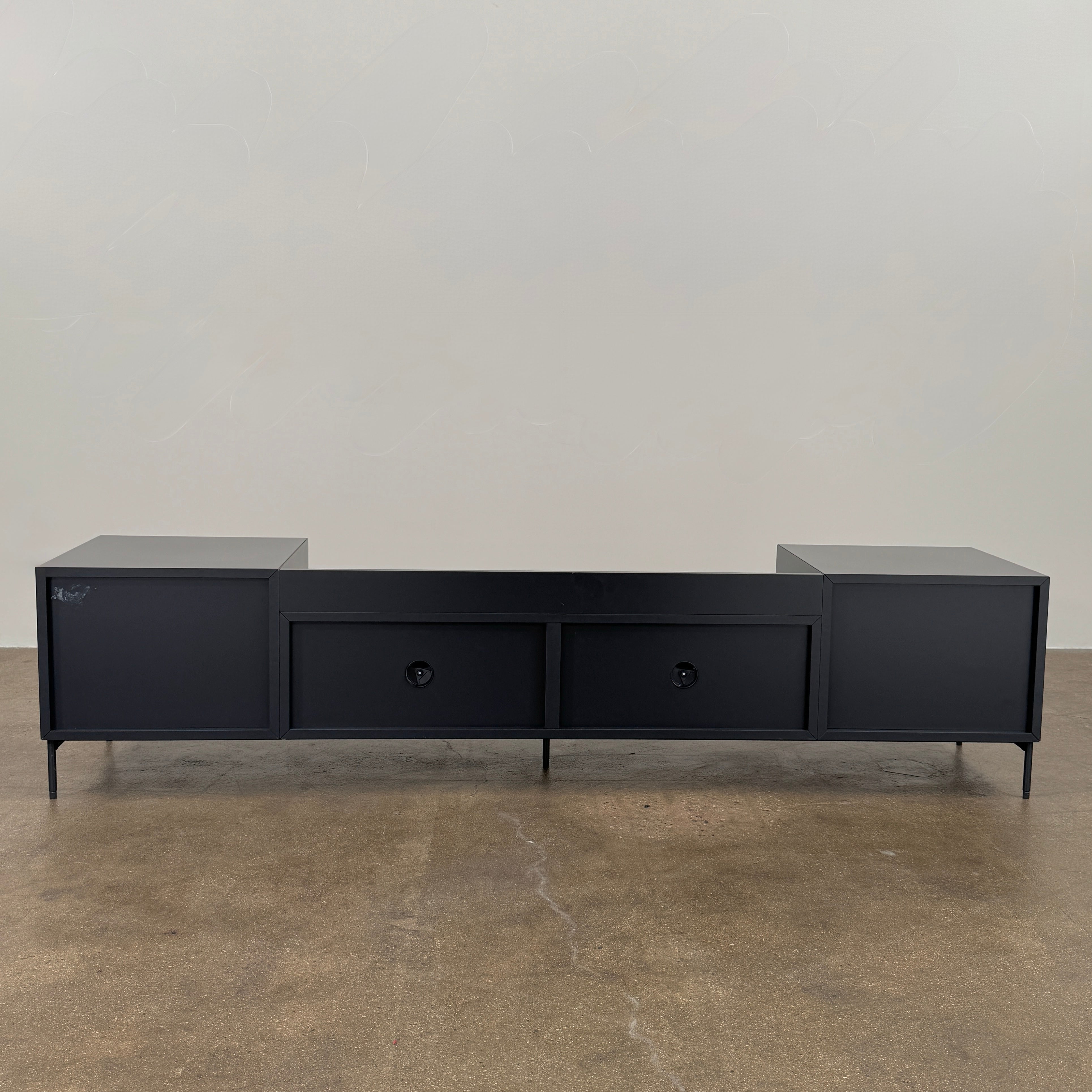 The Treku Lauki Media Unit by Treku features a black minimalist design with two closed side cabinets, two central drawers, an open shelf, and built-in cord management on slim metal legs—perfect for modern spaces.