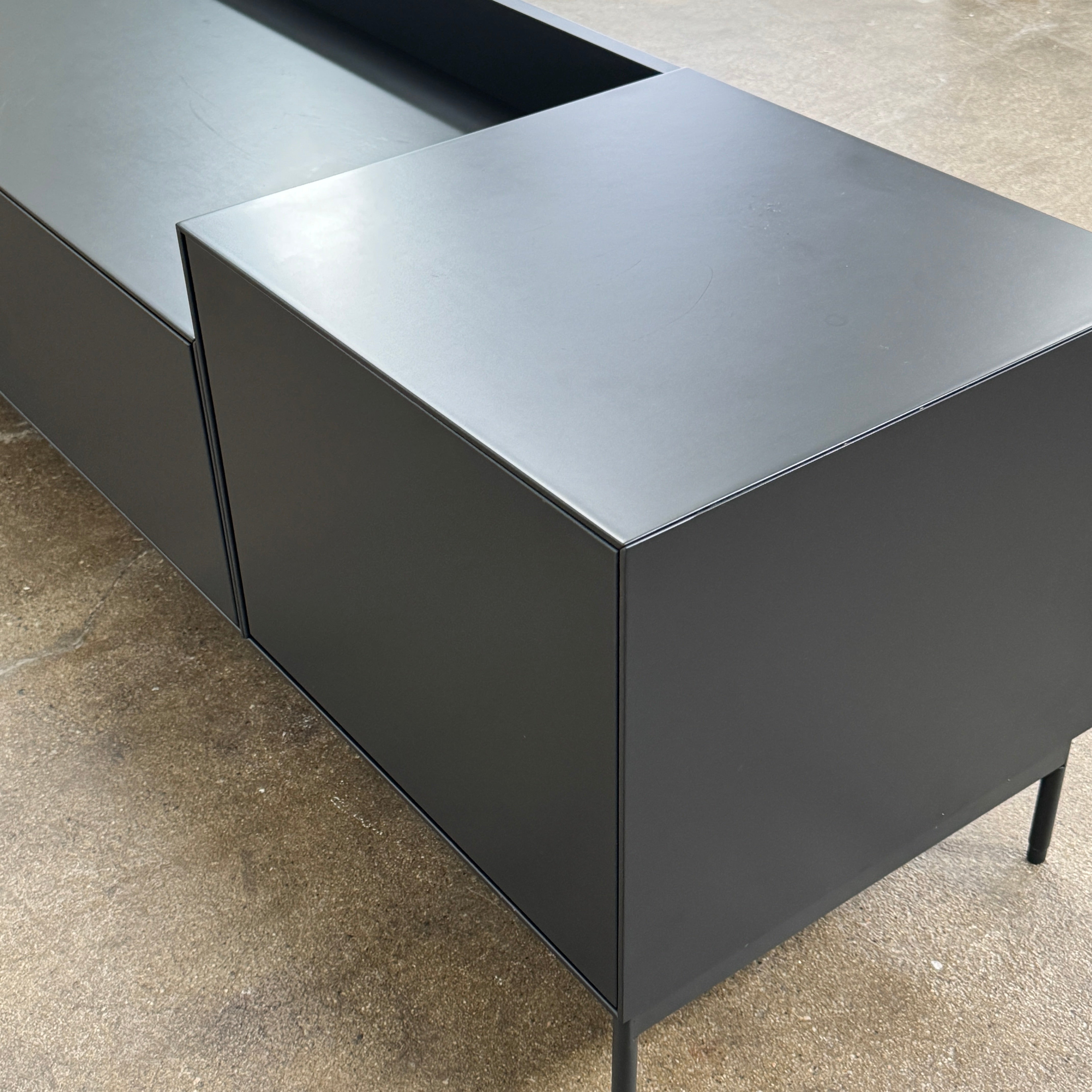 The Treku Lauki Media Unit by Treku features a black minimalist design with two closed side cabinets, two central drawers, an open shelf, and built-in cord management on slim metal legs—perfect for modern spaces.