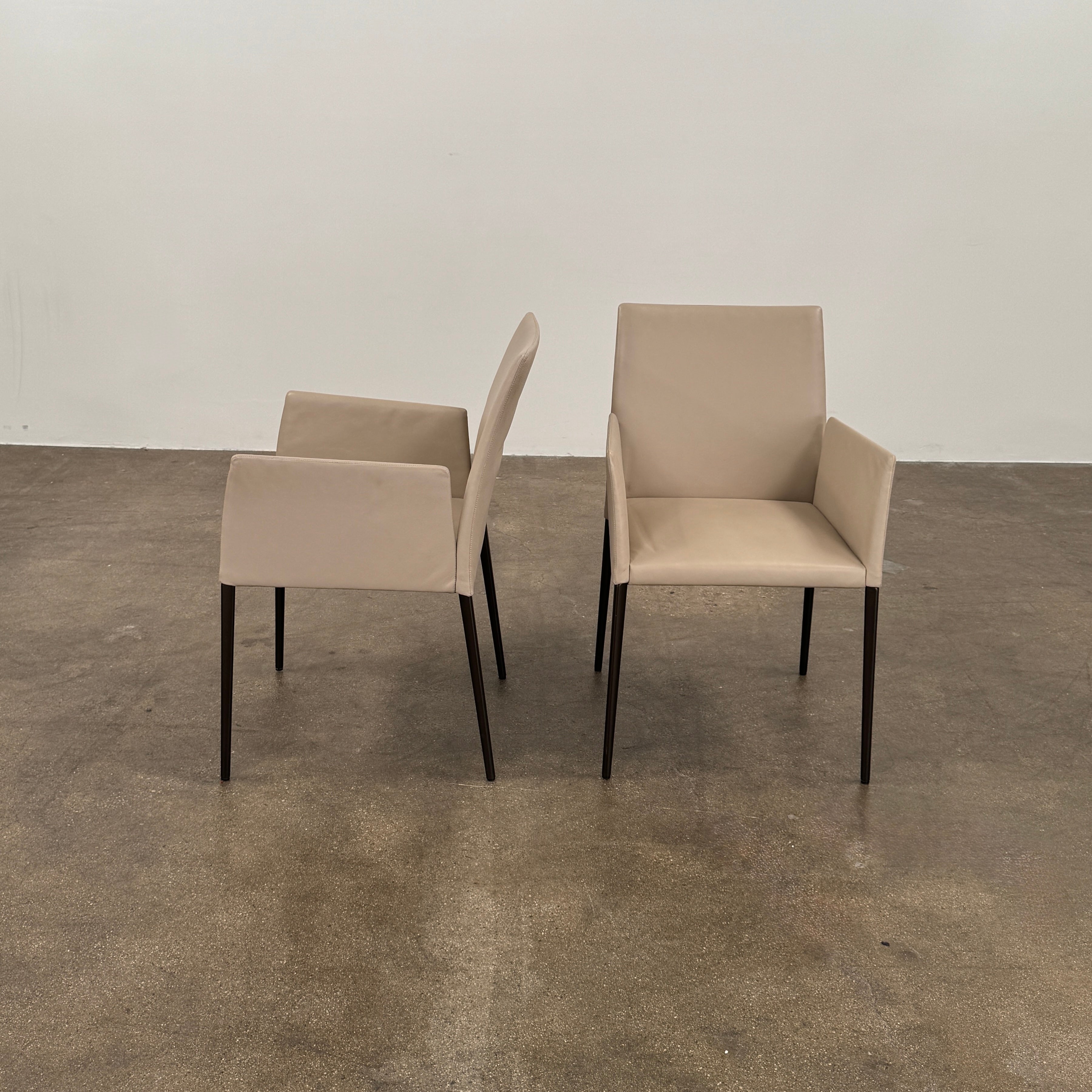 A set of Walter Knoll Deen Dining Chairs (2 armchairs, 8 side chairs) by Walter Knoll with beige upholstery and black legs are arranged in three rows on a brown concrete floor against a plain white wall.