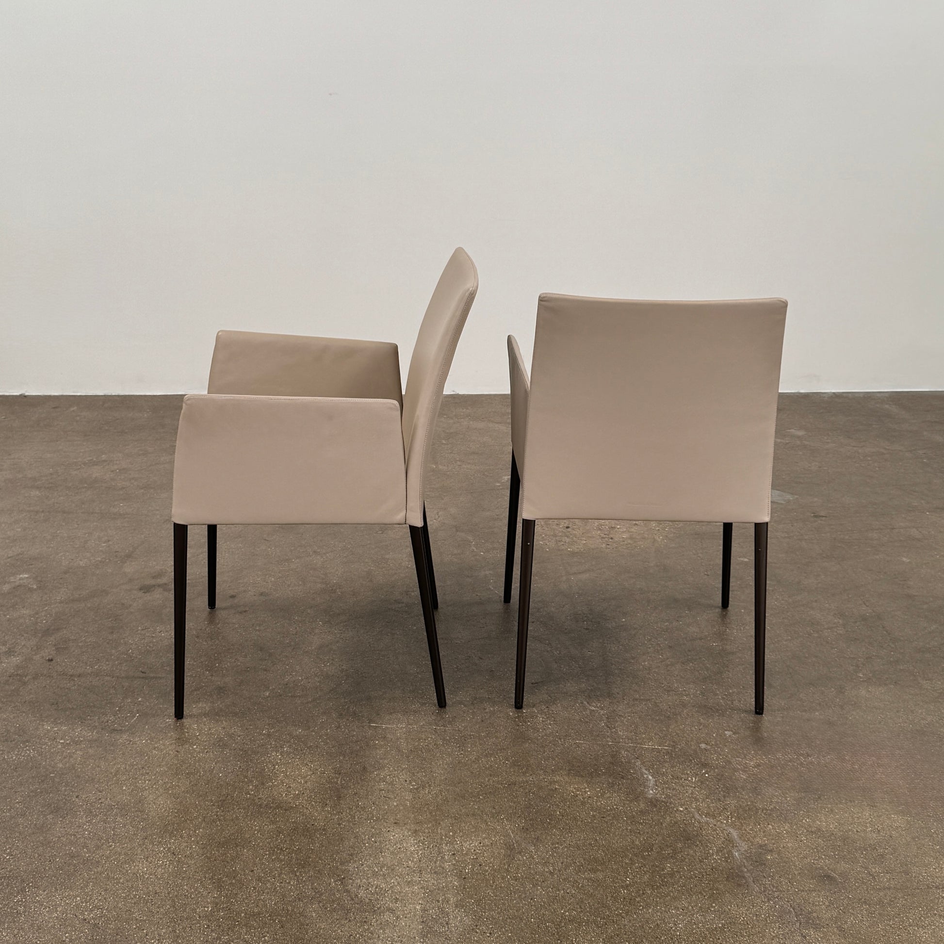 A set of Walter Knoll Deen Dining Chairs (2 armchairs, 8 side chairs) by Walter Knoll with beige upholstery and black legs are arranged in three rows on a brown concrete floor against a plain white wall.