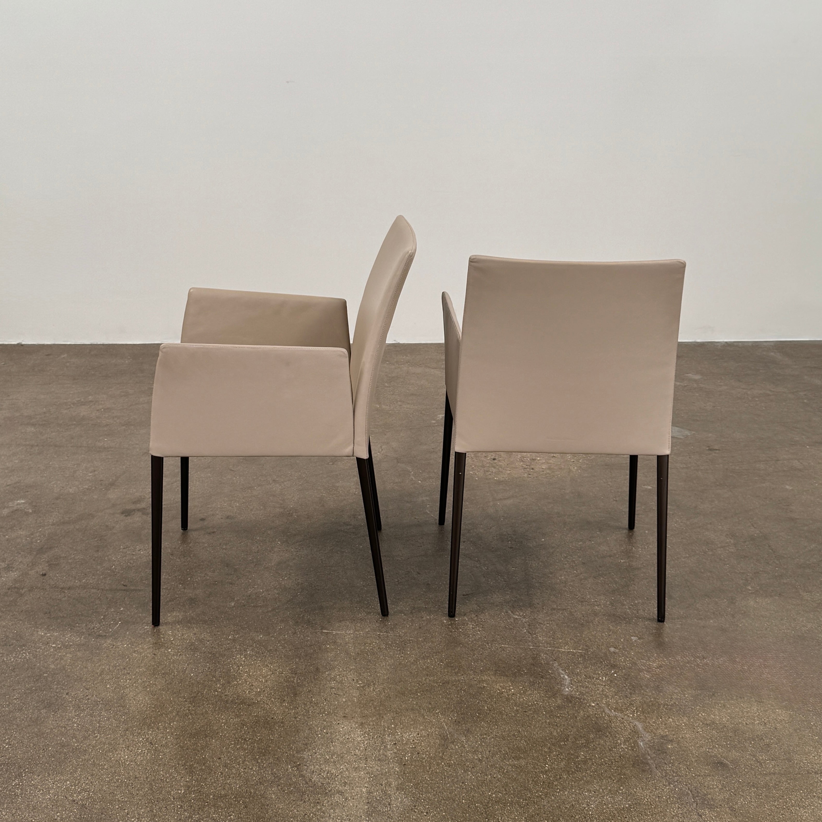 A set of Walter Knoll Deen Dining Chairs (2 armchairs, 8 side chairs) by Walter Knoll with beige upholstery and black legs are arranged in three rows on a brown concrete floor against a plain white wall.
