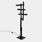 The Oluce LAS 376 LED Floor Lamp by Oluce features intersecting black rectangular panels on a flat base, with a visible power cord. Its sculptural design makes it a striking contemporary statement piece for any space.
