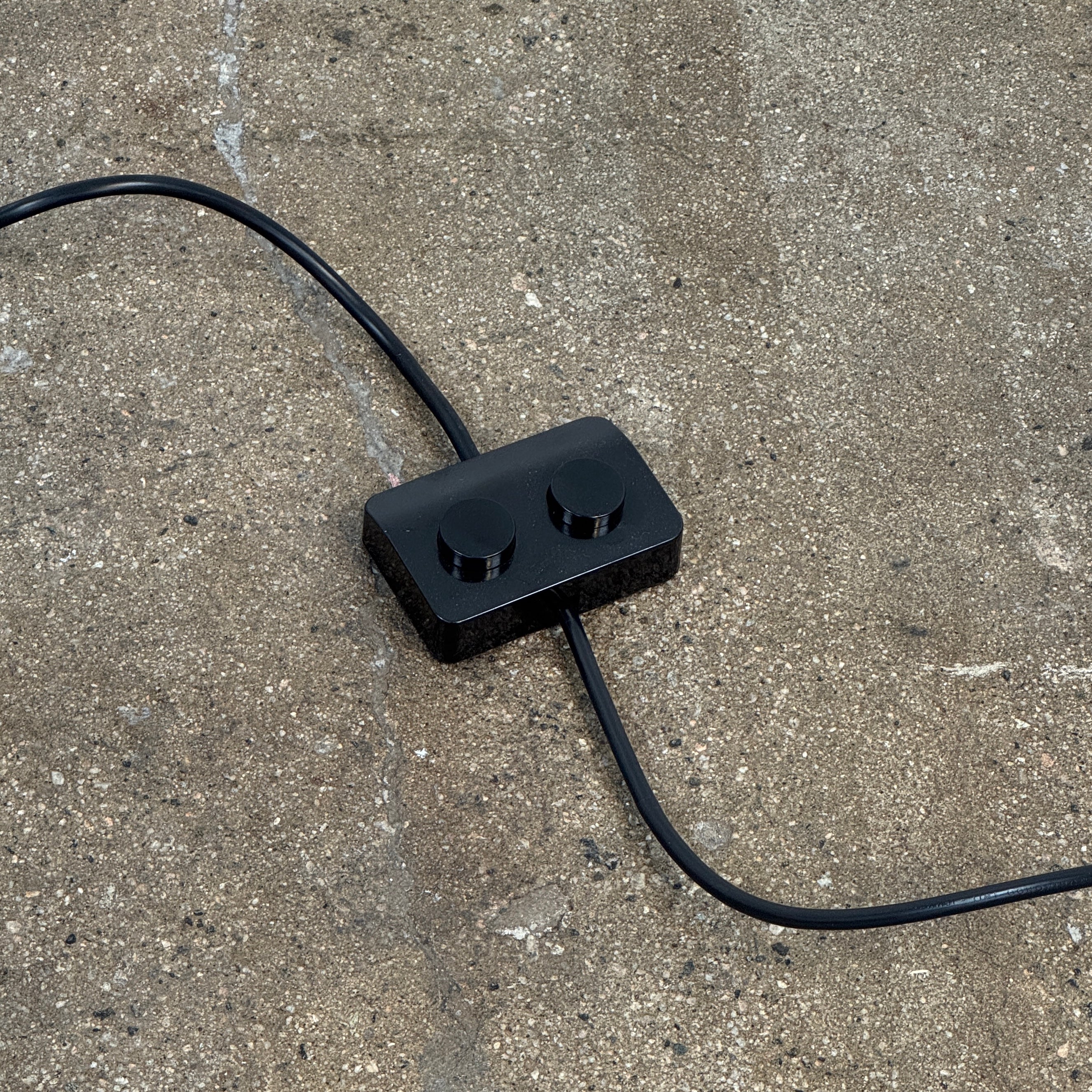 The Oluce LAS 376 LED Floor Lamp by Oluce features intersecting black rectangular panels on a flat base, with a visible power cord. Its sculptural design makes it a striking contemporary statement piece for any space.