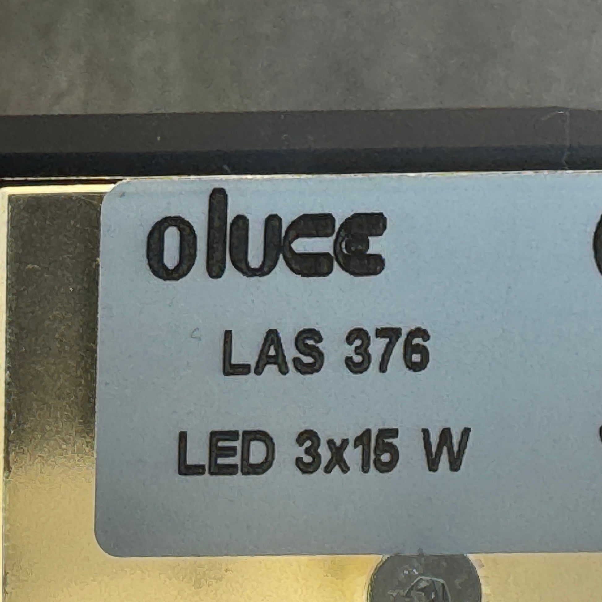 The Oluce LAS 376 LED Floor Lamp by Oluce features intersecting black rectangular panels on a flat base, with a visible power cord. Its sculptural design makes it a striking contemporary statement piece for any space.