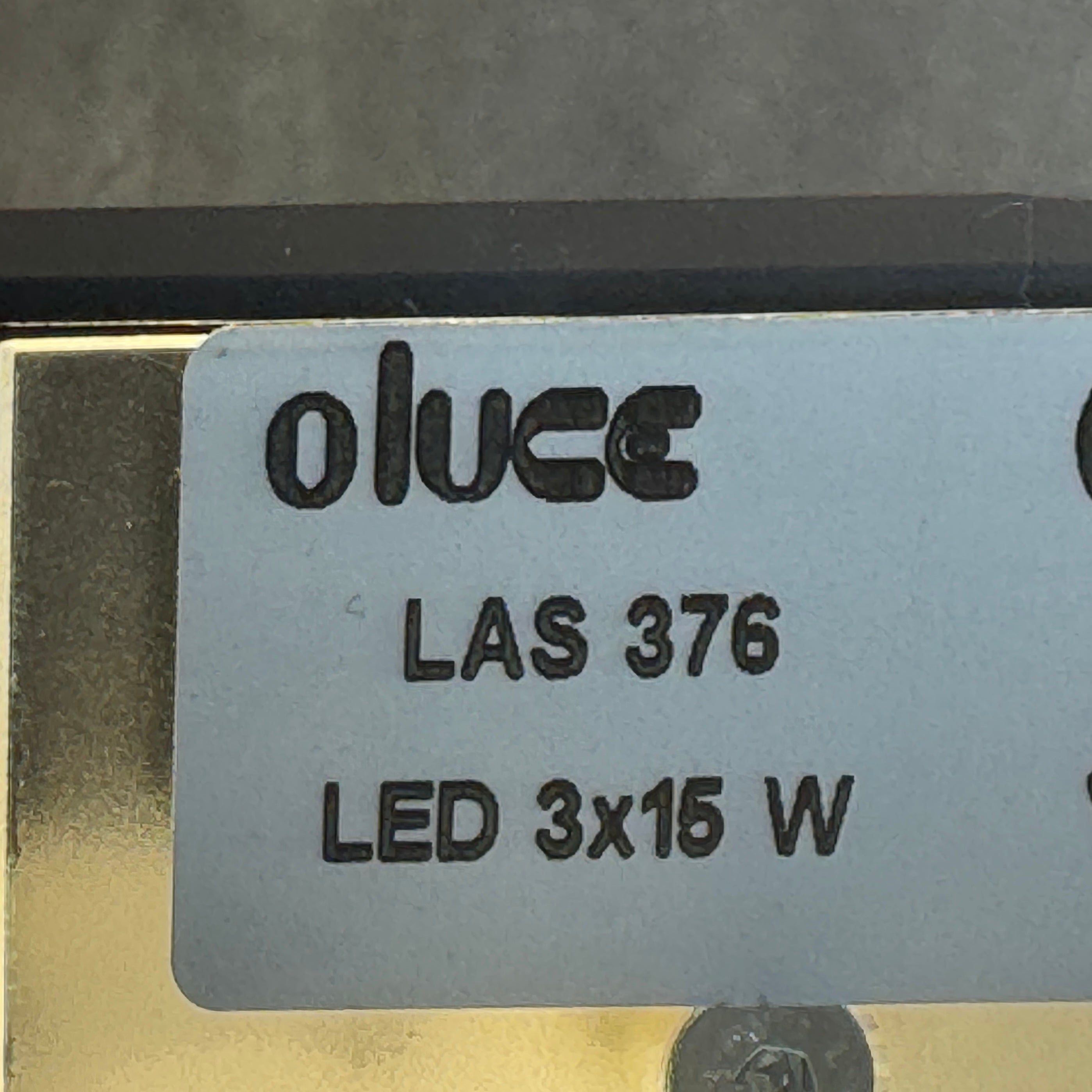 The Oluce LAS 376 LED Floor Lamp by Oluce features intersecting black rectangular panels on a flat base, with a visible power cord. Its sculptural design makes it a striking contemporary statement piece for any space.