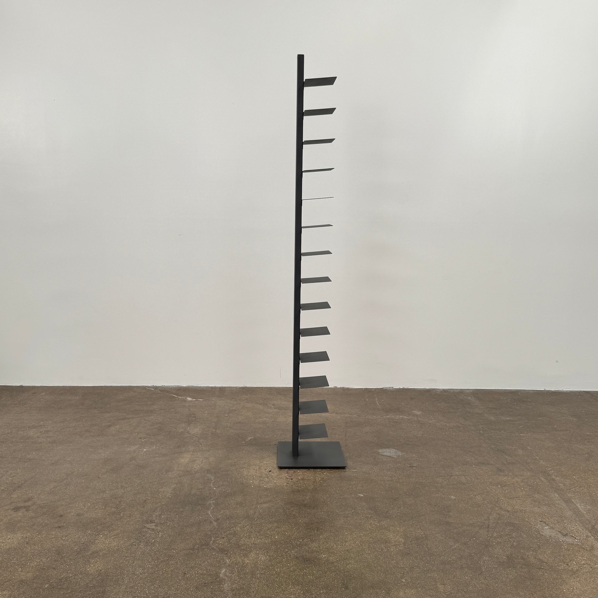 The DWR Story Bookcase by DWR is a tall, black, vertical metal bookcase with evenly spaced shelves and a square base—ideal for small-room storage and shown against a plain light background.