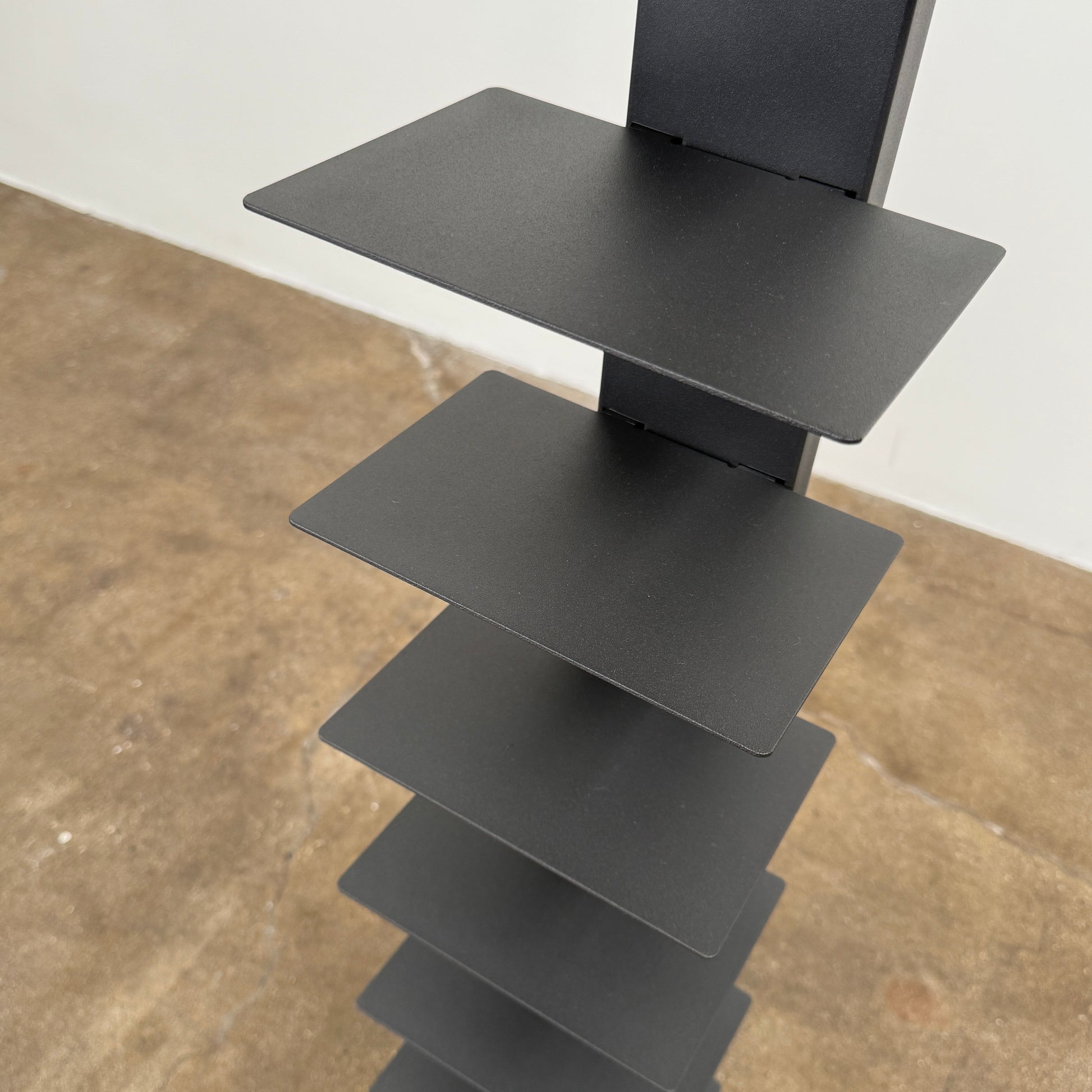 The DWR Story Bookcase by DWR is a tall, black, vertical metal bookcase with evenly spaced shelves and a square base—ideal for small-room storage and shown against a plain light background.