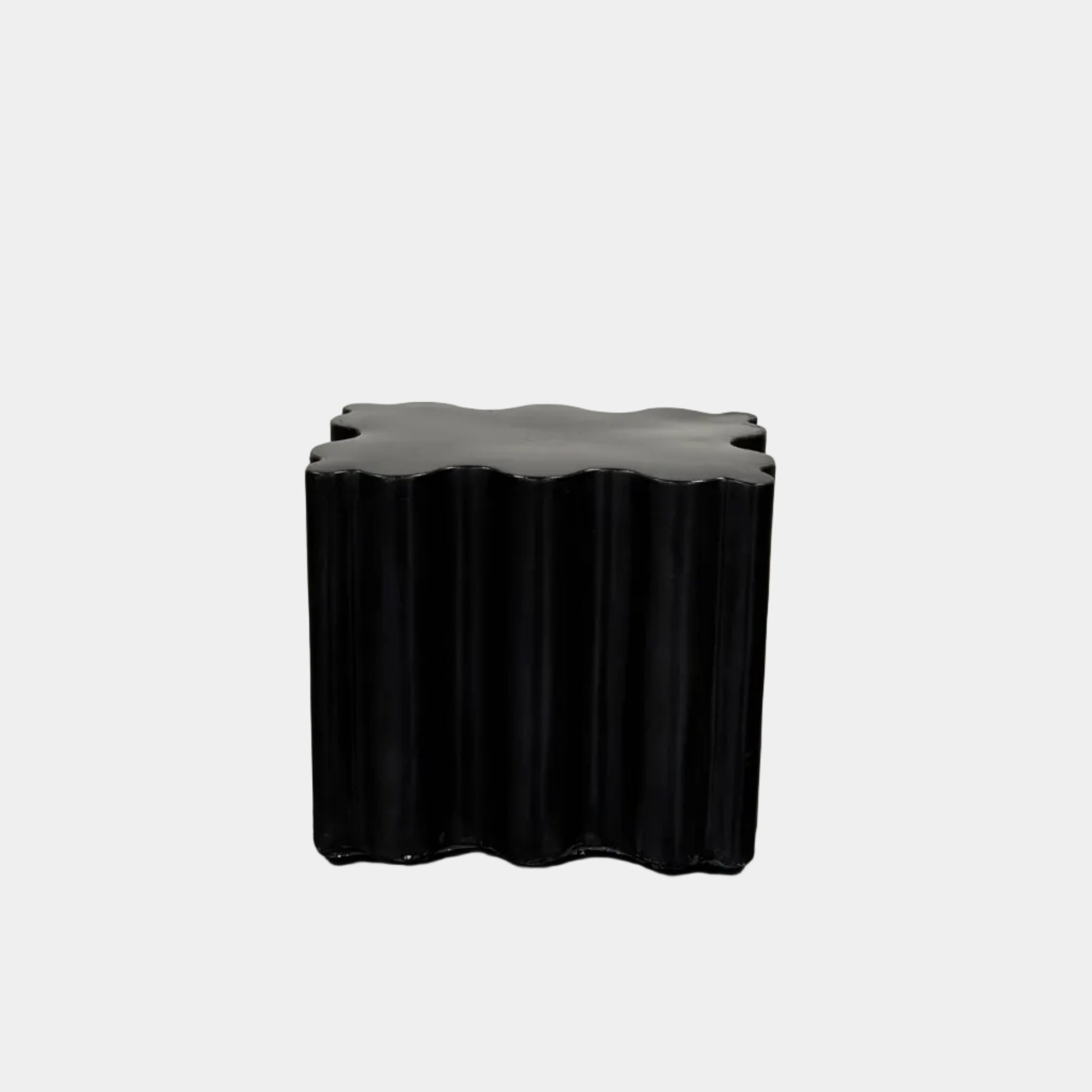 The Patrick Cain Cloud Table Black Concrete, a black wavy-edged cube by Patrick Cain, sits on a concrete floor against a plain white wall.