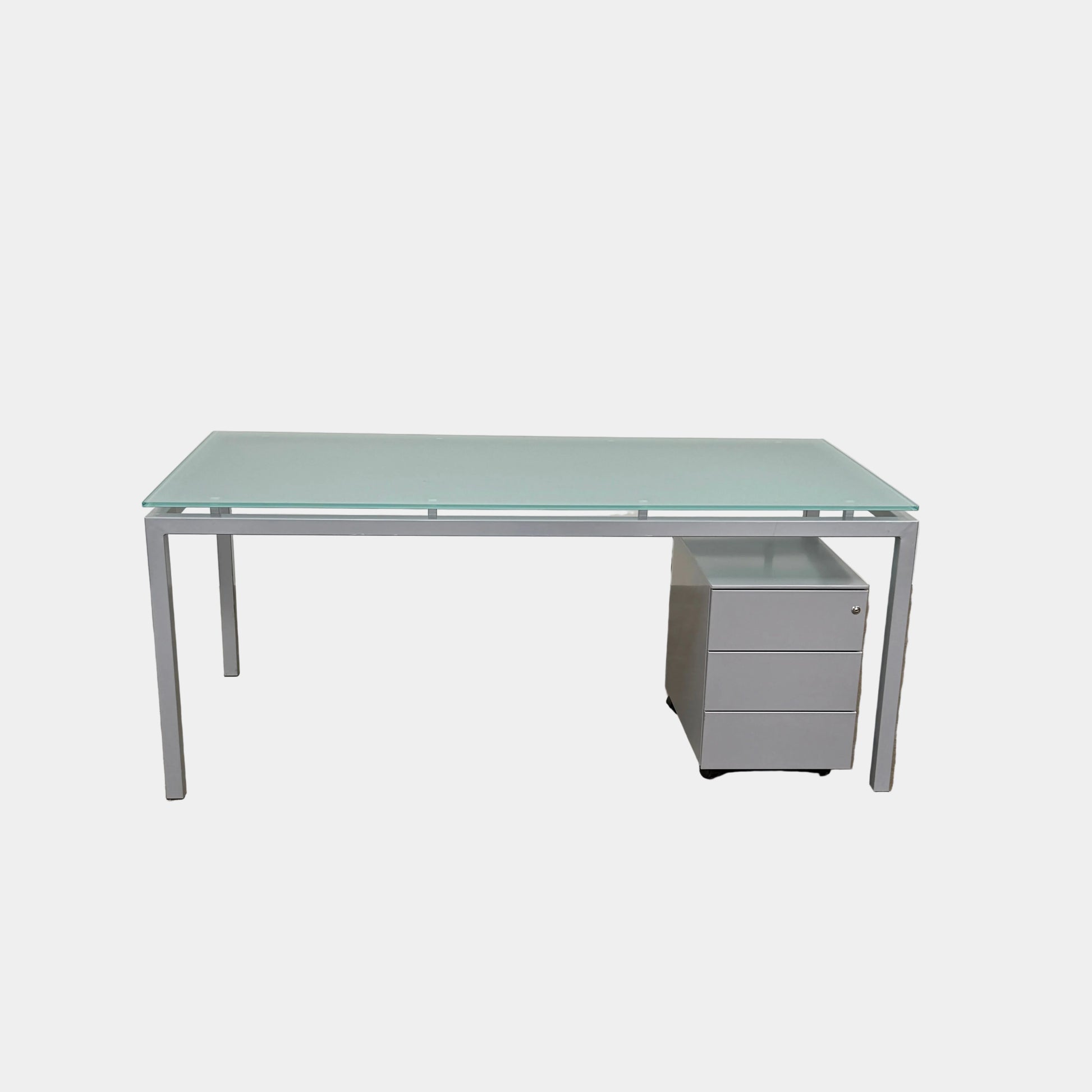 The DWR Tavolo Glass Desk with Chest of drawers by DWR features a sleek glass top, metal legs, and a mobile chest of drawers beneath—perfect for a contemporary office setup.