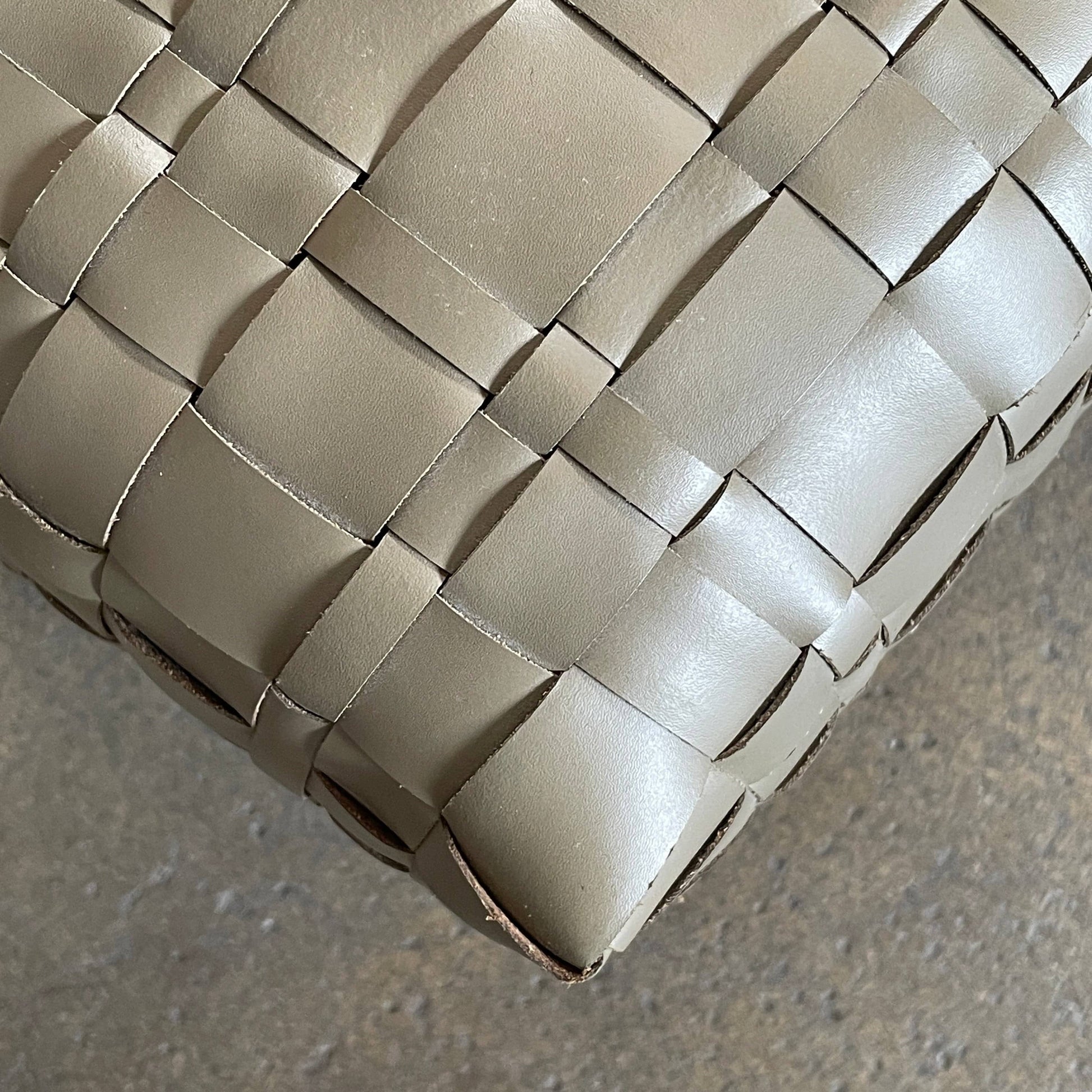 A square, beige Flexform Bangkok Ottoman with a woven leather pattern and four short metal legs evokes the stylish charm of Bangkok.