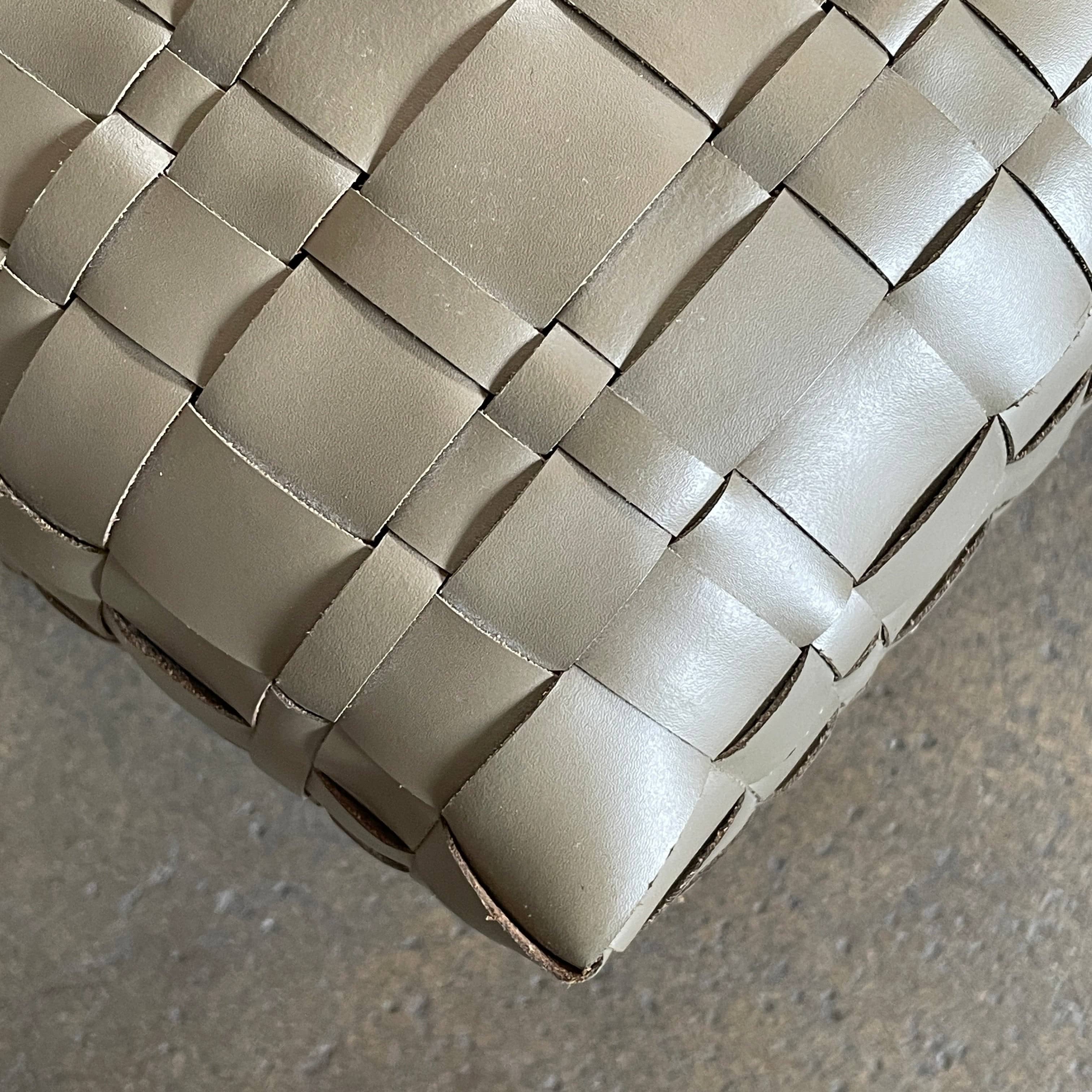 A square, beige Flexform Bangkok Ottoman with a woven leather pattern and four short metal legs evokes the stylish charm of Bangkok.