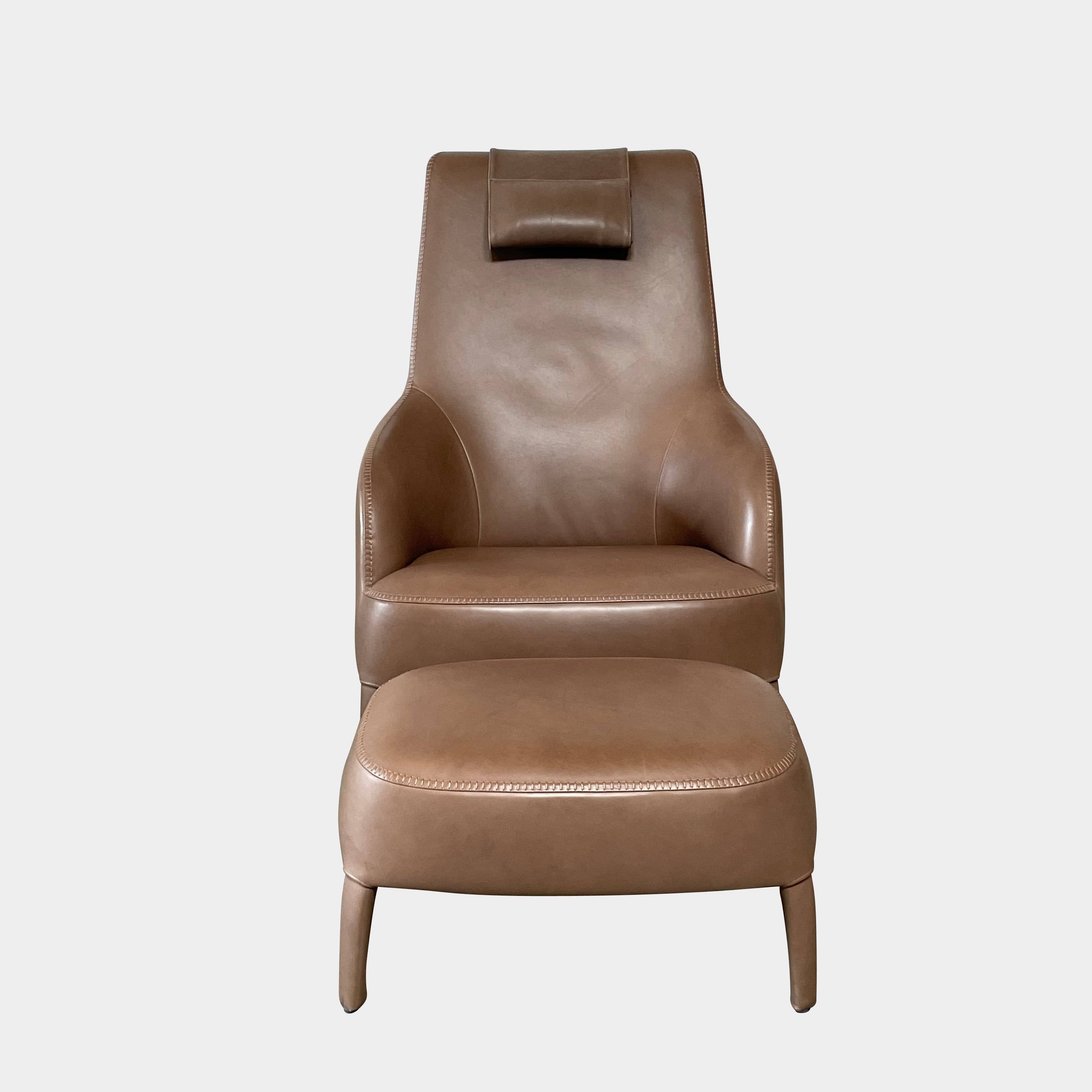 A brown leather armchair with a high backrest and curved arms, showcasing classic leather upholstery, is paired with a matching ottoman, both resting on thin legs. This sophisticated set embodies the elegant style of Maxalto's Maxalto Febo High Back Lounge Chair and Ottoman collection.