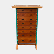 The Joseph Schwarte Tall Chest of Drawers by Artist features nine drawers, teal vertical side supports, black rectangular pulls, and a flat top—postmodern-inspired and shown against a plain background.
