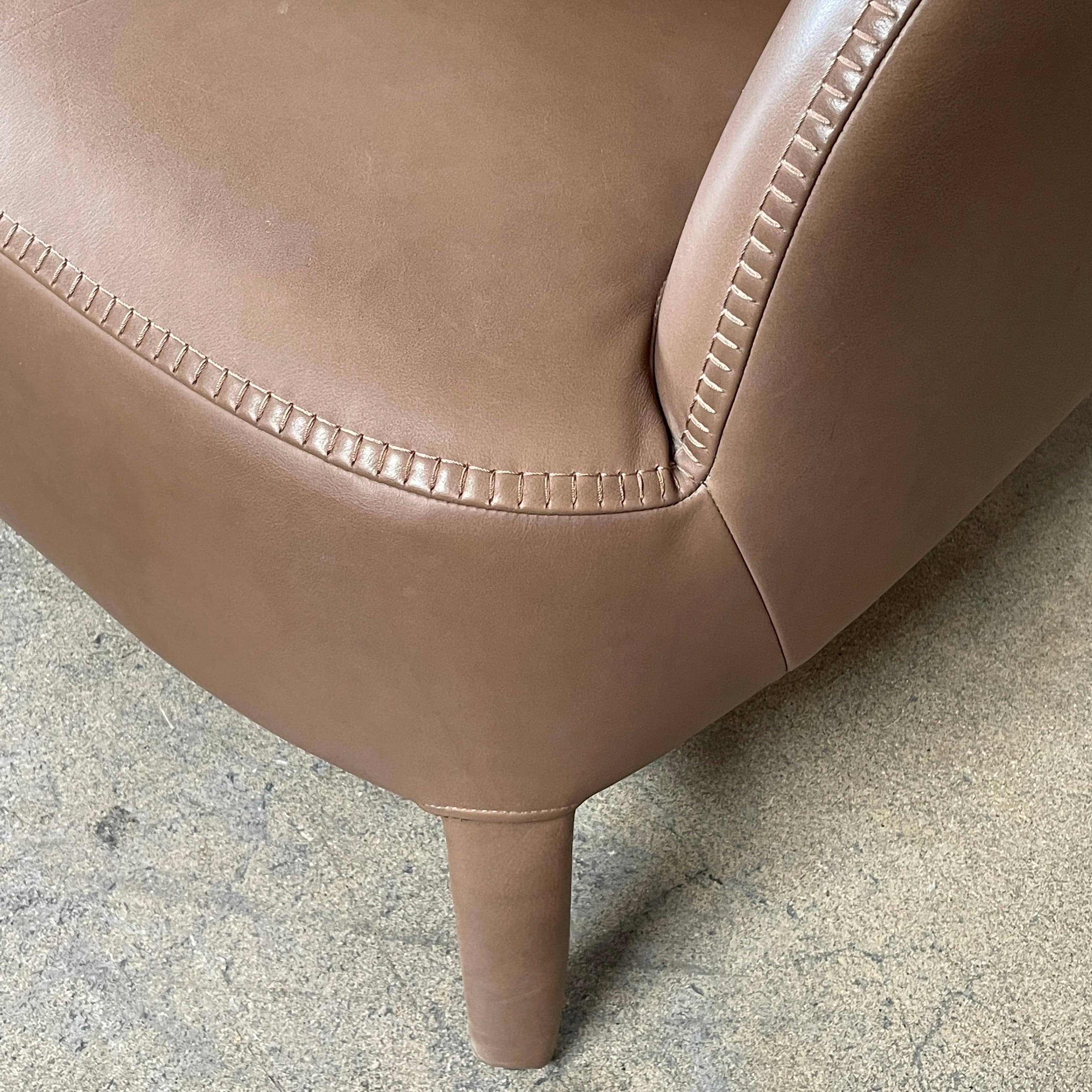 A brown leather armchair with a high backrest and curved arms, showcasing classic leather upholstery, is paired with a matching ottoman, both resting on thin legs. This sophisticated set embodies the elegant style of Maxalto's Maxalto Febo High Back Lounge Chair and Ottoman collection.