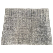 An 8'x10' rectangular DWR Luna Rug in gray with a subtle textured pattern is placed on a concrete floor against a white wall.