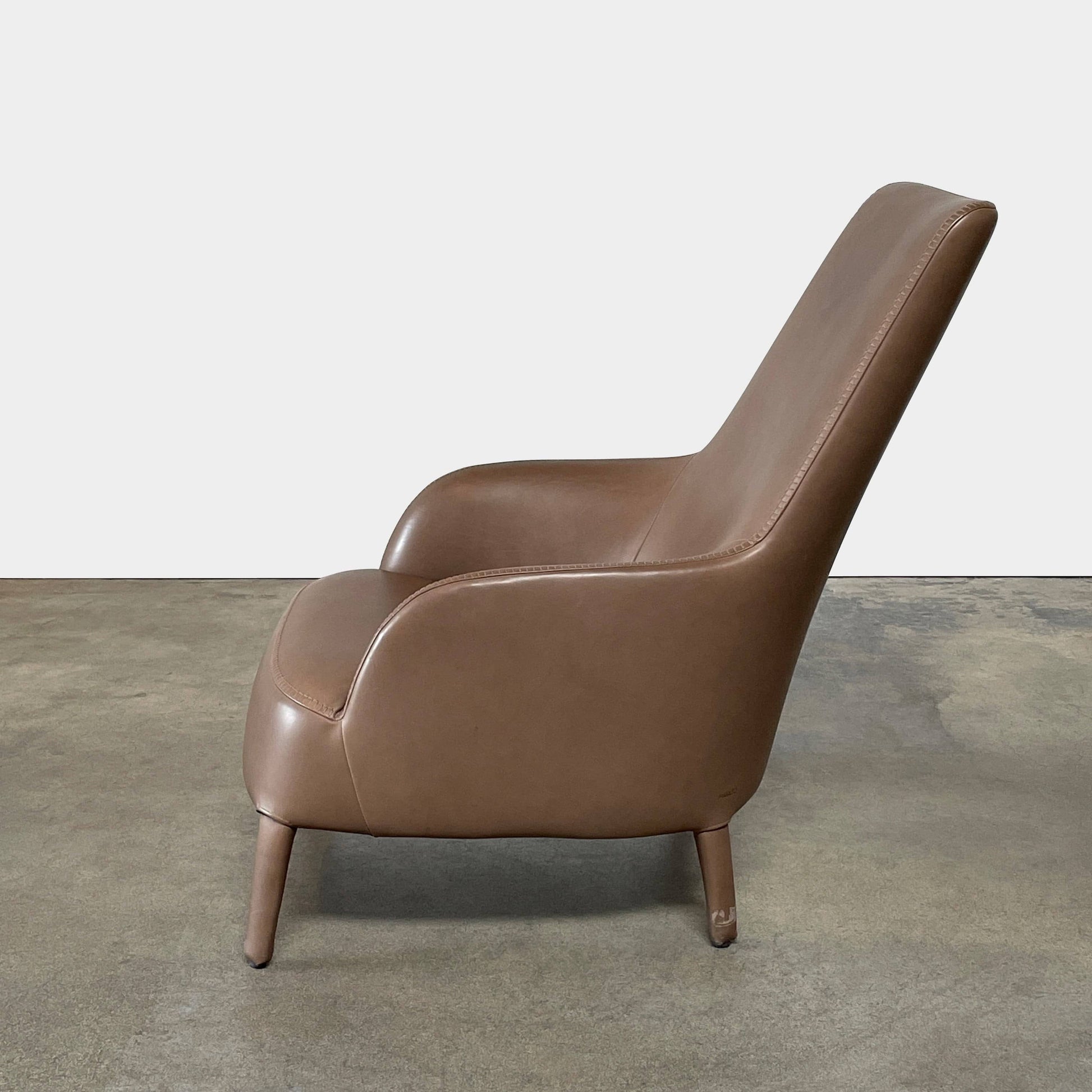 A brown leather armchair with a high backrest and curved arms, showcasing classic leather upholstery, is paired with a matching ottoman, both resting on thin legs. This sophisticated set embodies the elegant style of Maxalto's Maxalto Febo High Back Lounge Chair and Ottoman collection.