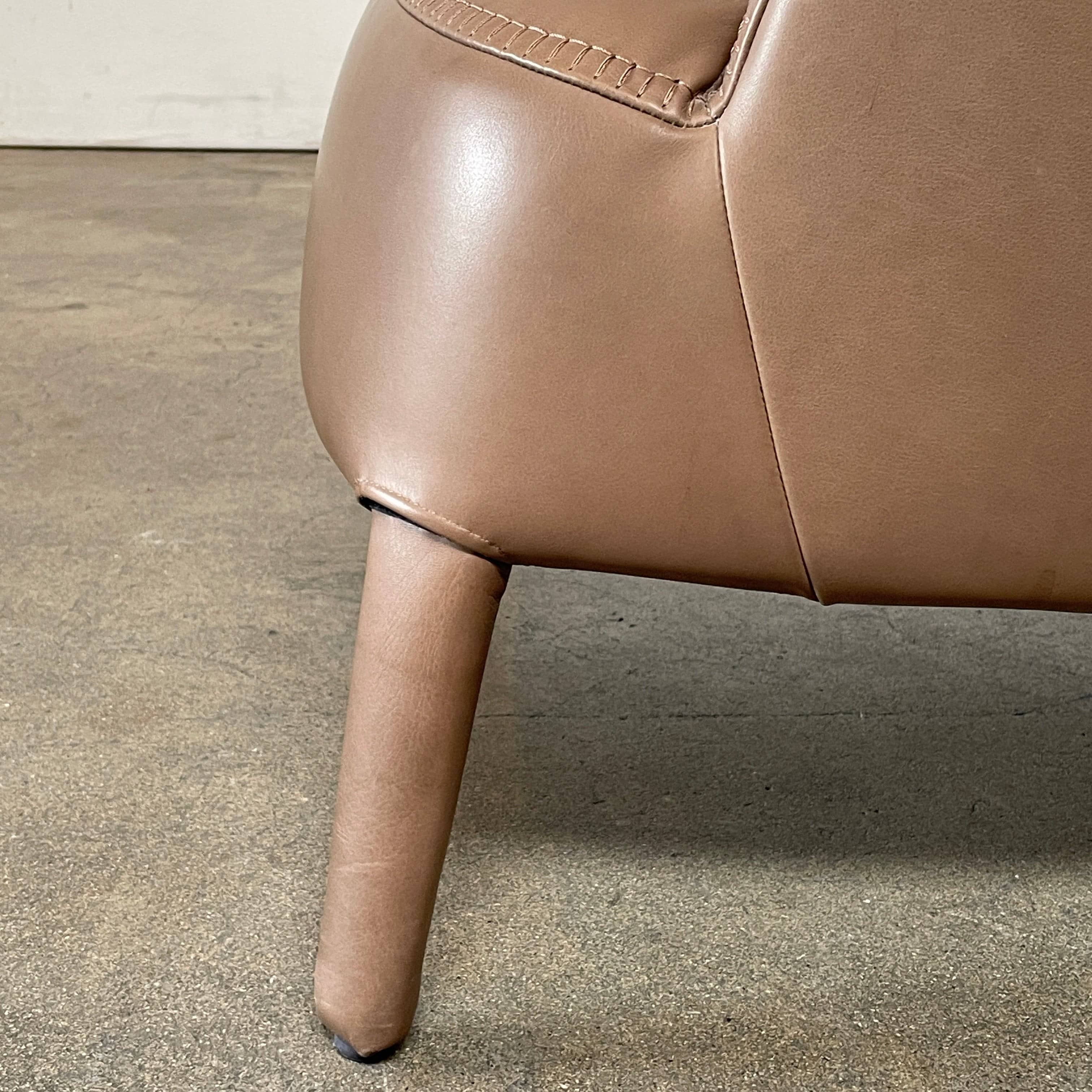 A brown leather armchair with a high backrest and curved arms, showcasing classic leather upholstery, is paired with a matching ottoman, both resting on thin legs. This sophisticated set embodies the elegant style of Maxalto's Maxalto Febo High Back Lounge Chair and Ottoman collection.
