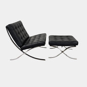 The Vintage DWR Barcelona Black Leather Chair & Ottoman by DWR features button-tufted cushions and chrome X-shaped legs, taking inspiration from the iconic Barcelona Chair, all presented against a plain white background.