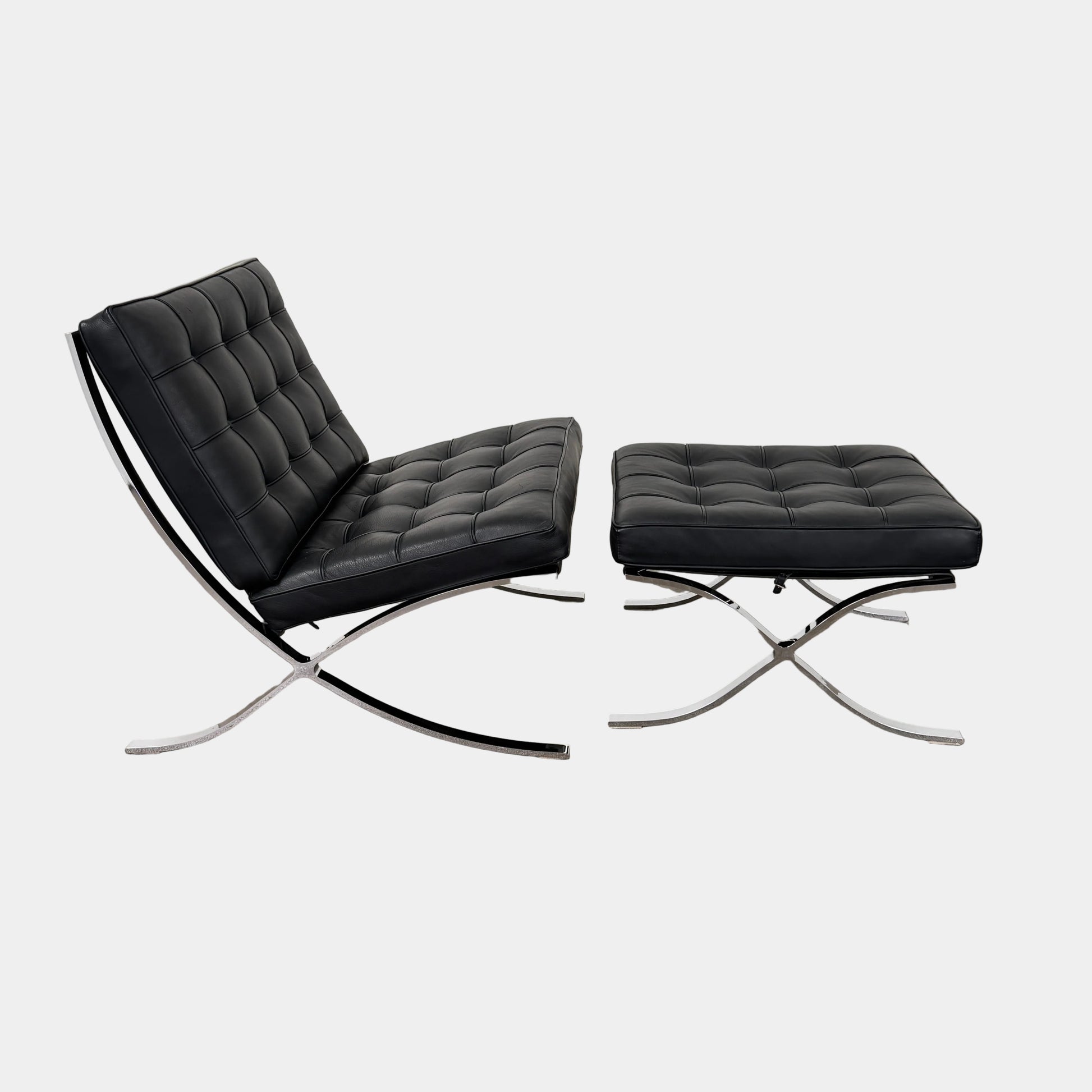 The Vintage DWR Barcelona Black Leather Chair & Ottoman by DWR features button-tufted cushions and chrome X-shaped legs, taking inspiration from the iconic Barcelona Chair, all presented against a plain white background.
