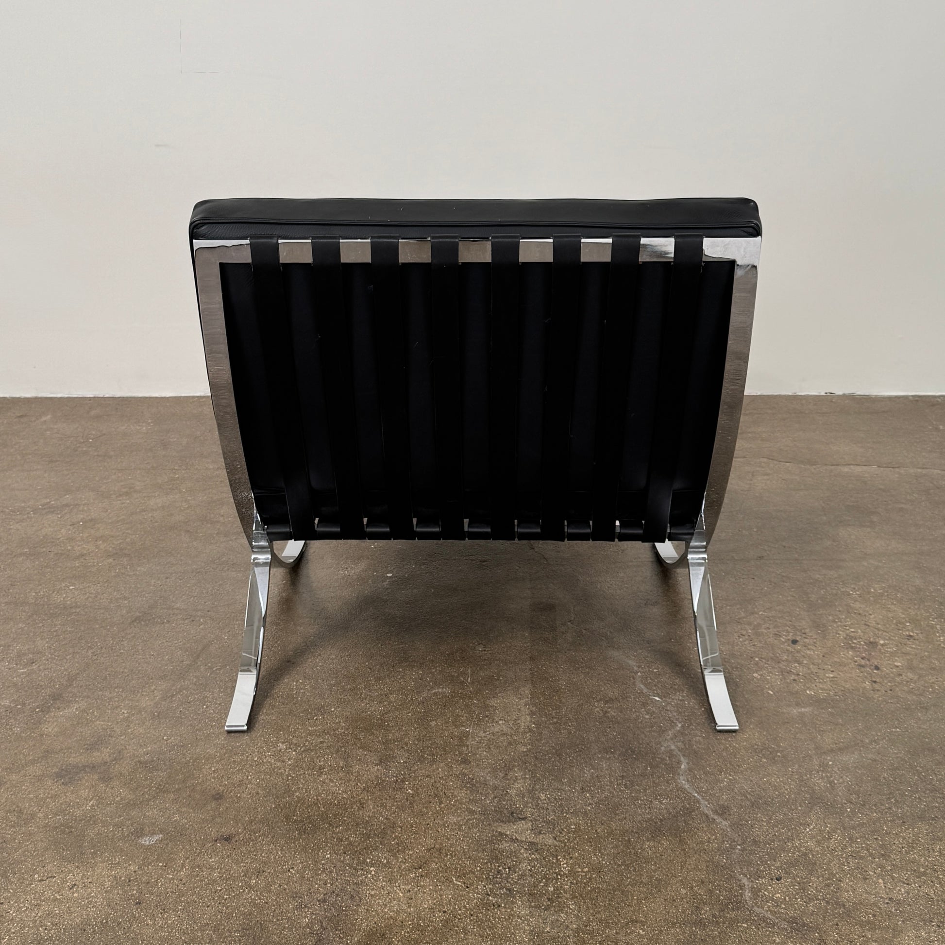The Vintage DWR Barcelona Black Leather Chair & Ottoman by DWR features button-tufted cushions and chrome X-shaped legs, taking inspiration from the iconic Barcelona Chair, all presented against a plain white background.